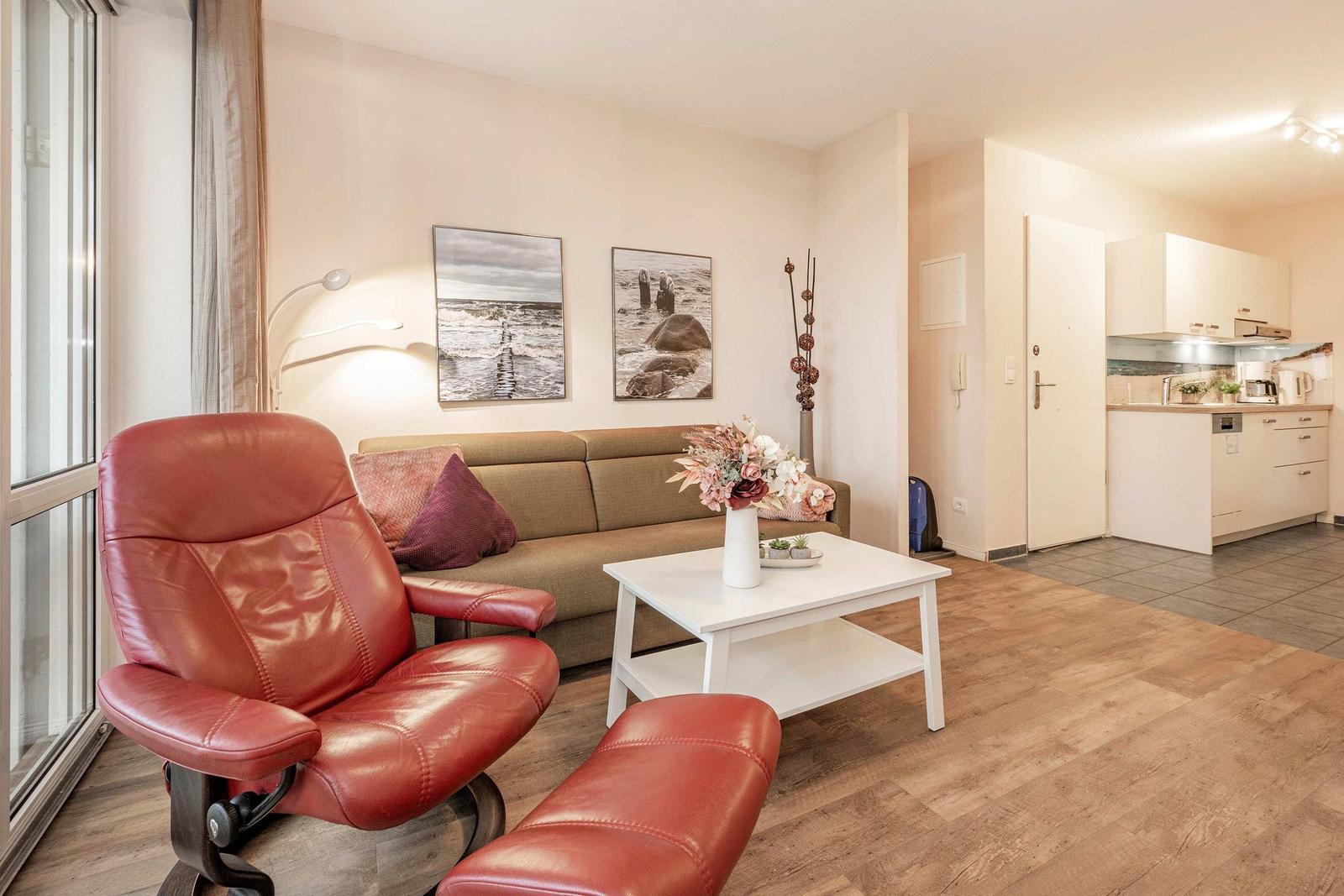 Wohnzimmer mit Sofa, rotem Sessel und Küchenbereich im Hintergrund.