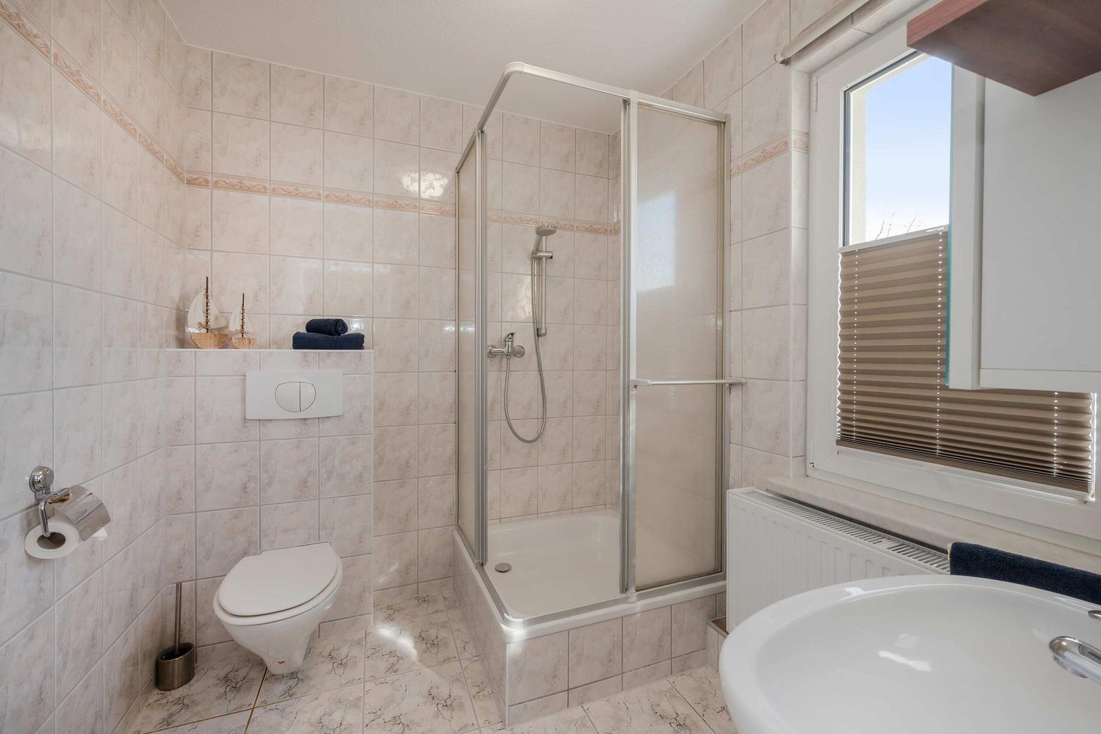 Badezimmer mit Dusche, Toilette und Waschbecken. Fenster mit Jalousie.