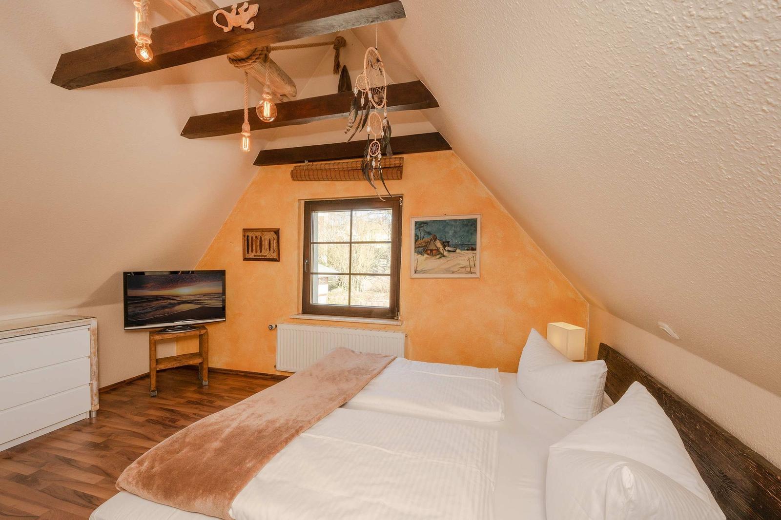 Schlafzimmer mit Dachschrägen, Bett, Fernseher und Fenster.