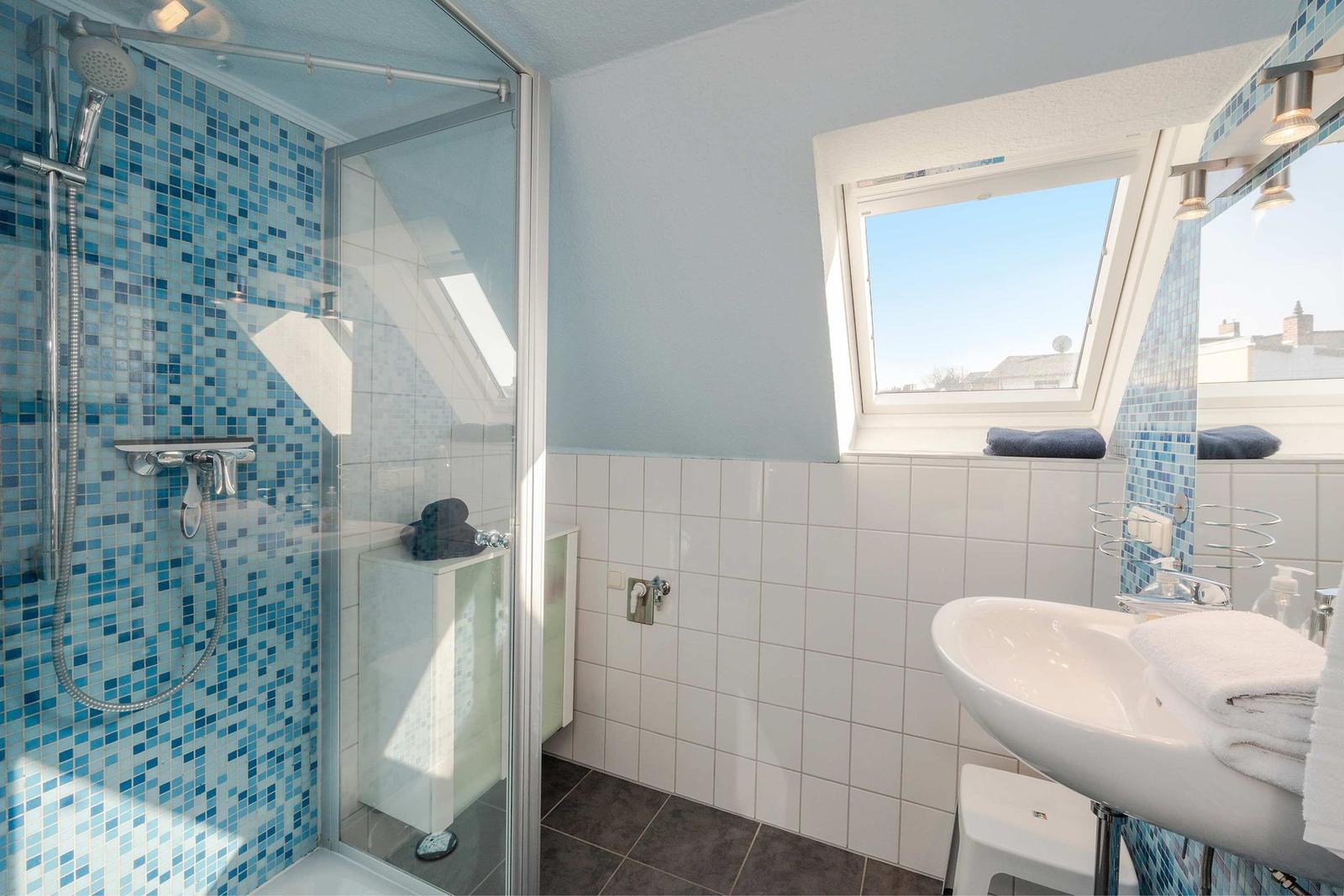 Bad mit Dusche, Waschbecken und Dachfenster. Wände mit blauen Fliesen.