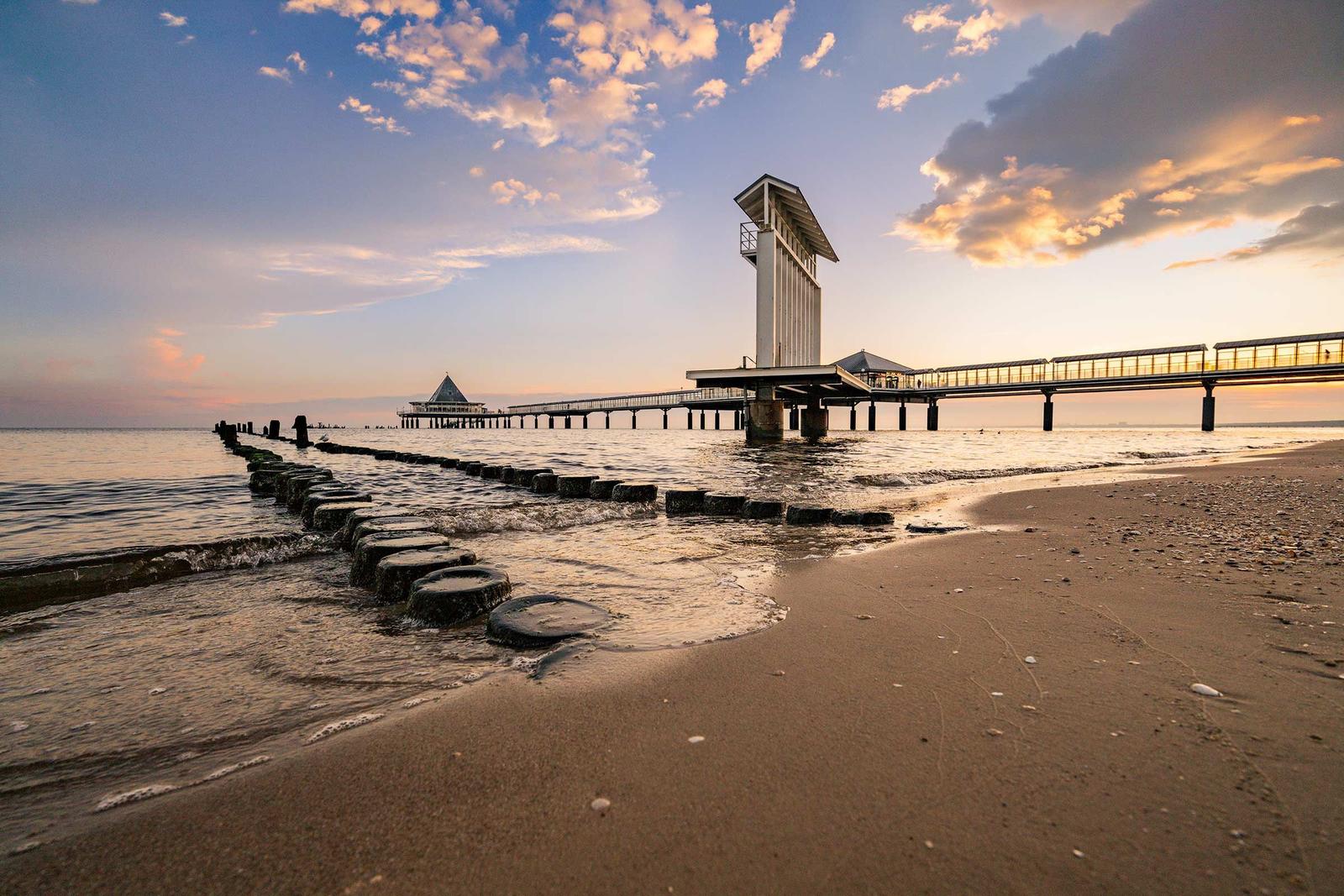 Strand mit Steinen, Pier und Leuchtturm bei Sonnenuntergang