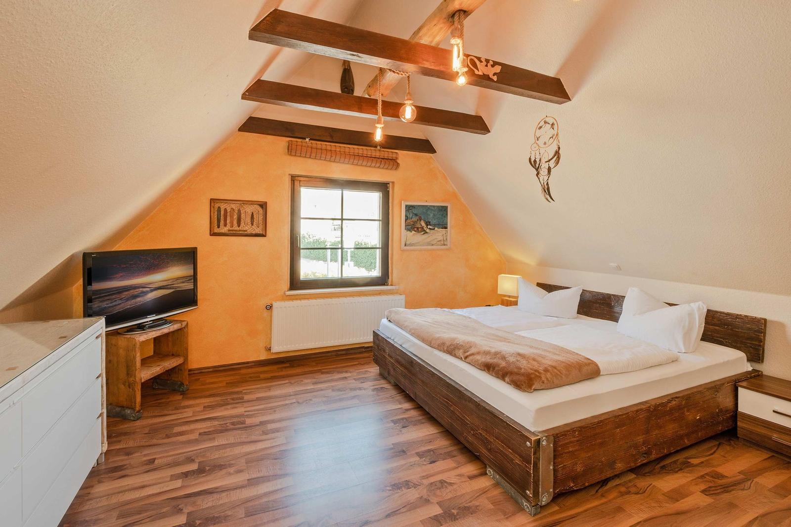 Schlafzimmer mit Dachschrägen, Holzbett, TV und Fenster.