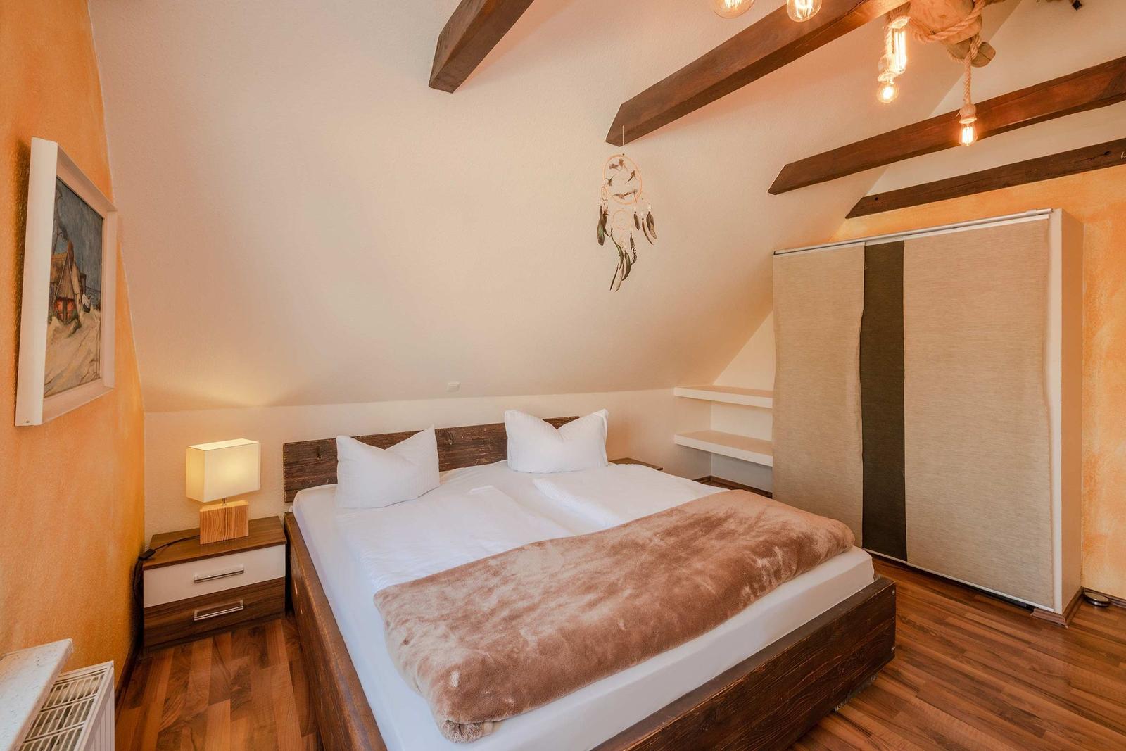 Schlafzimmer mit Doppelbett, Holzboden und Holzbalken an der Decke.