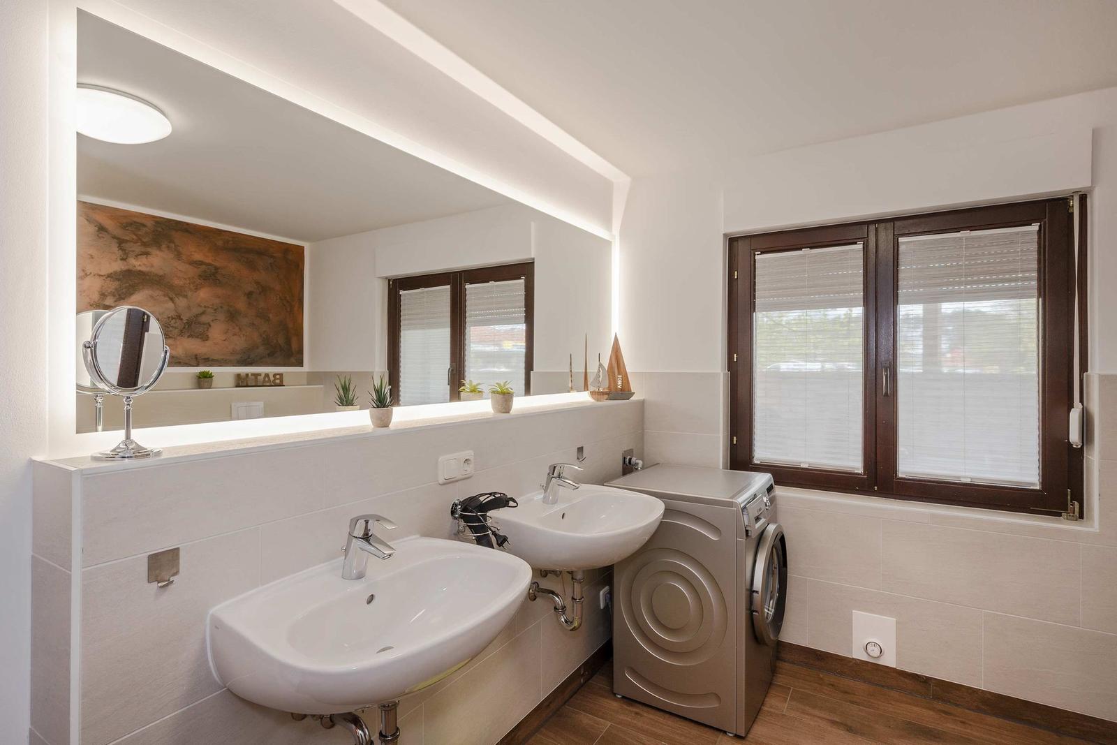 Badezimmer mit zwei Waschbecken, Spiegel und Waschmaschine.
