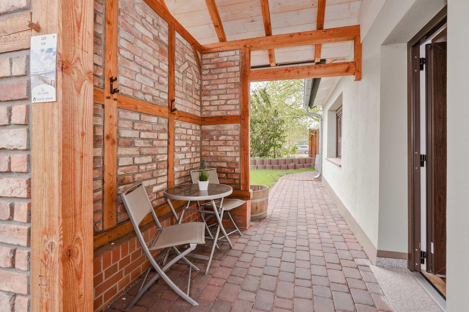Terrasse mit Tisch, Stühlen und Pflanze unter Holzkonstruktion. Zufahrt zum Haus.