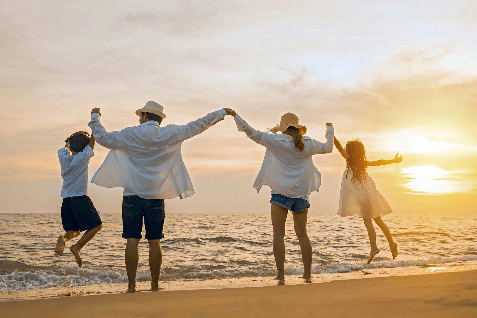 Familie springt am Strand bei Sonnenuntergang zusammengehalten.