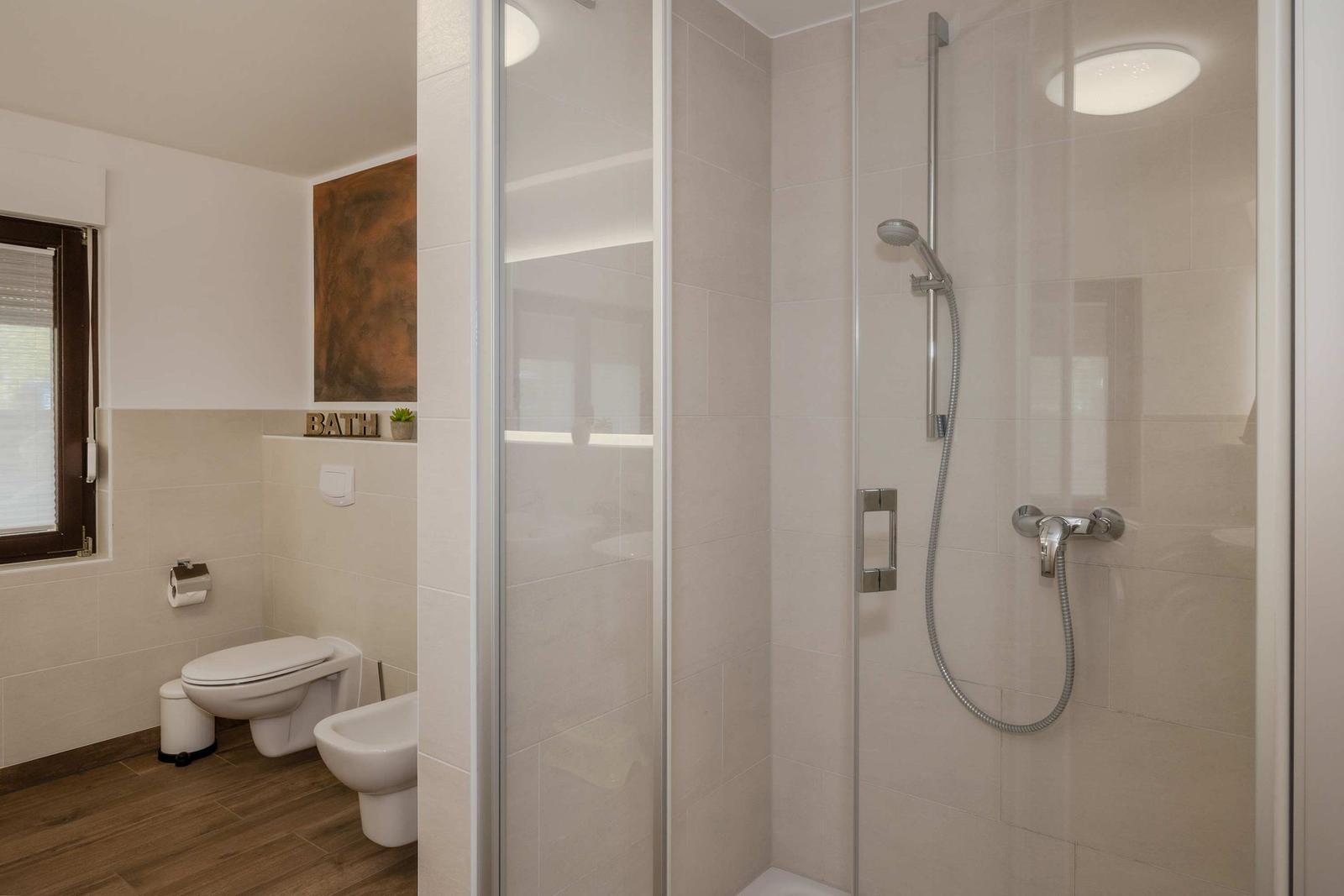 Bad mit Dusche, WC und Bidet. Holzfußboden und Fenster mit Jalousie.