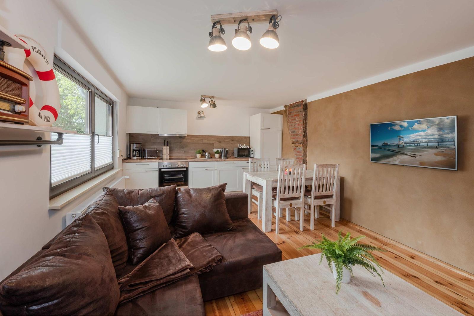 Wohnküche mit braunem Sofa, Esstisch und Fernseher an der Wand.