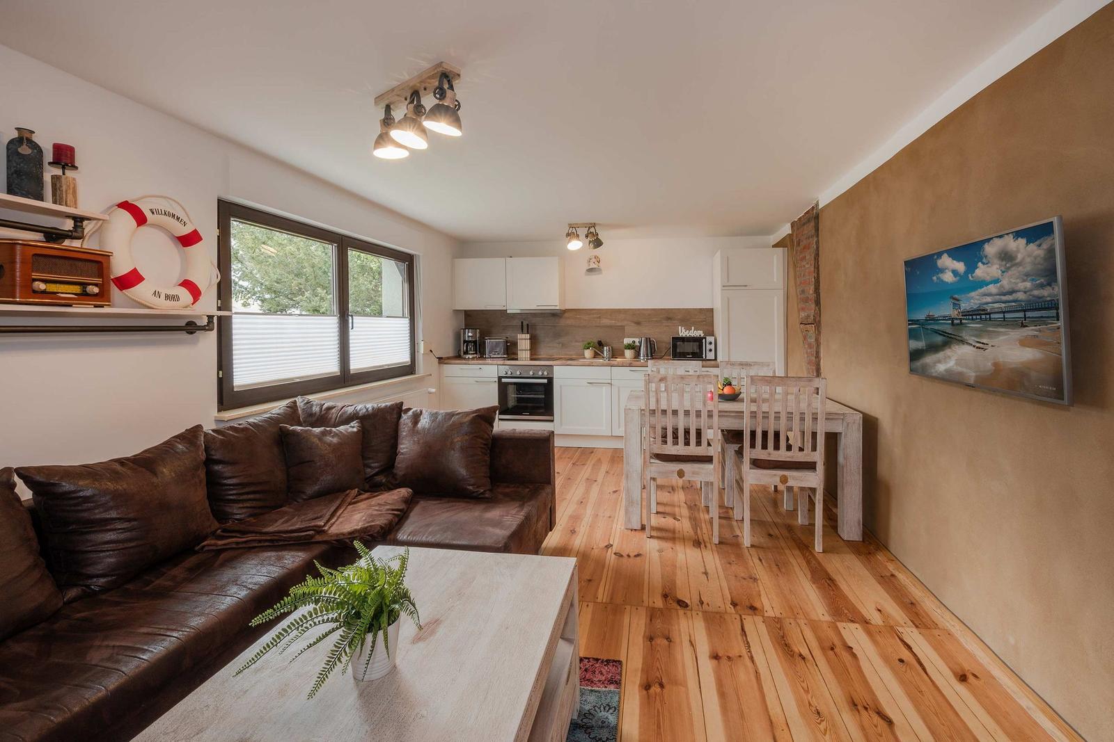Wohnzimmer mit Sofa, Esstisch und Küche. Holzboden und Wandbild.