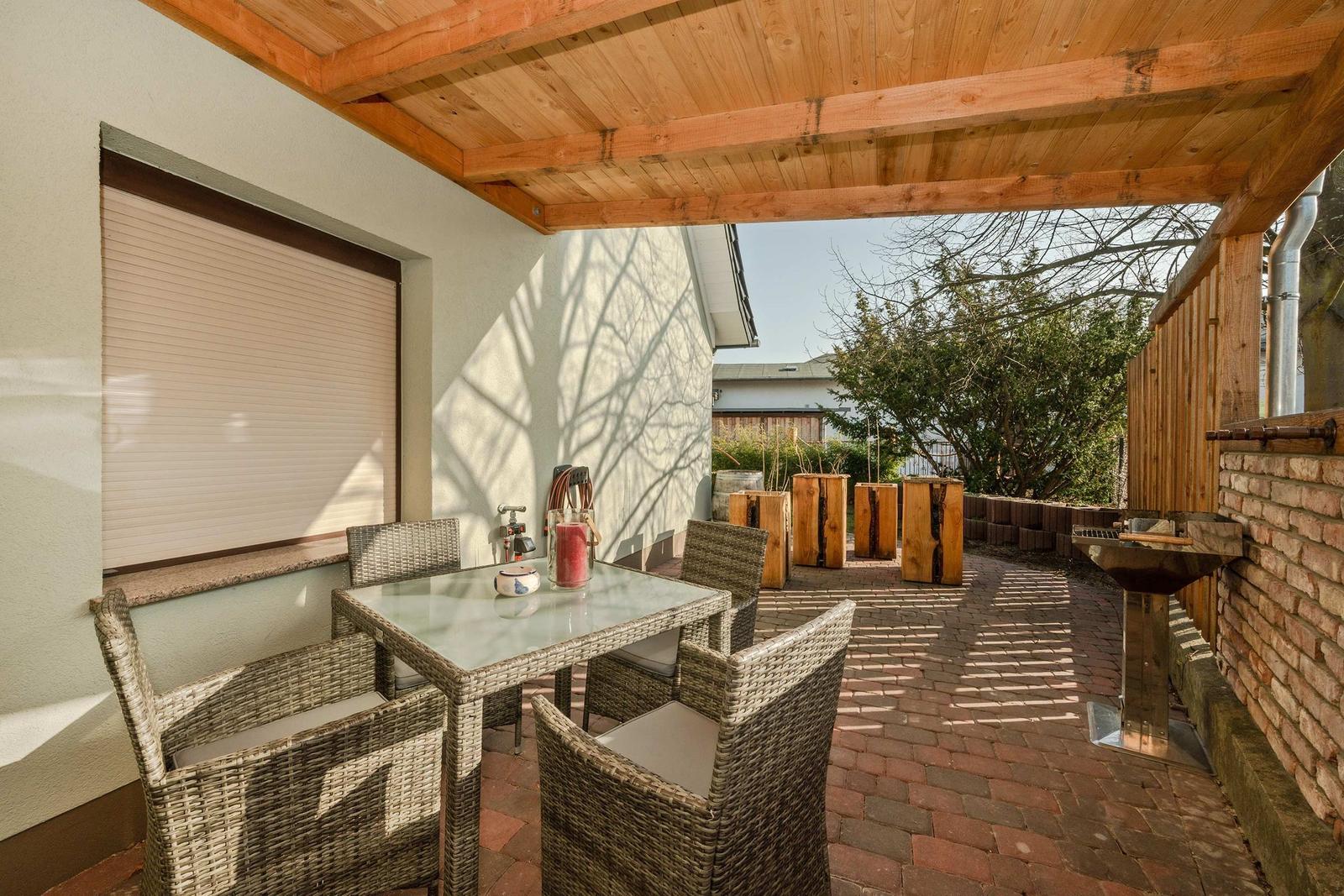 Terrasse mit Sitzgruppe, Grill und Holzüberdachung. Pflasterboden und Holzwände.