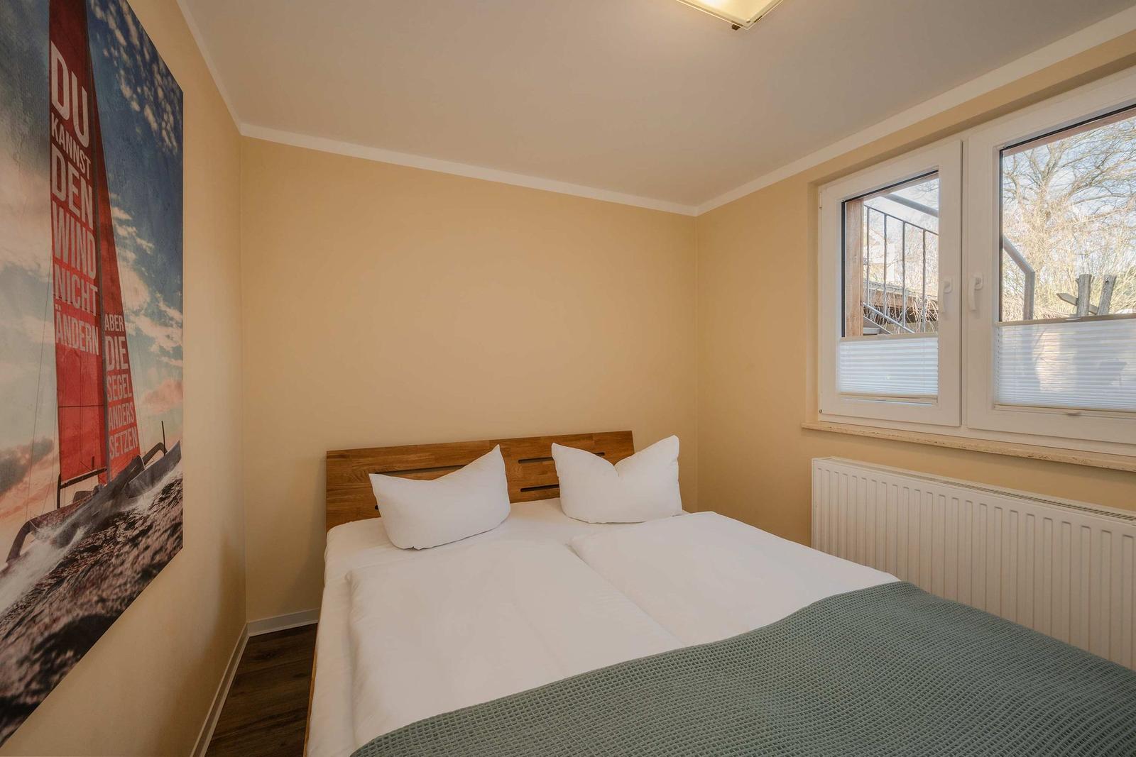 Schlafzimmer mit Doppelbett, Fenster und Wandbild mit Segelboot.