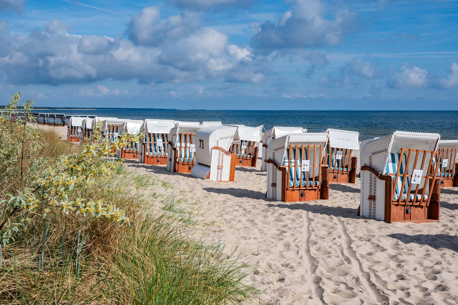 Strandkörbe auf Sandstrand mit Blick auf Meer und Himmel.