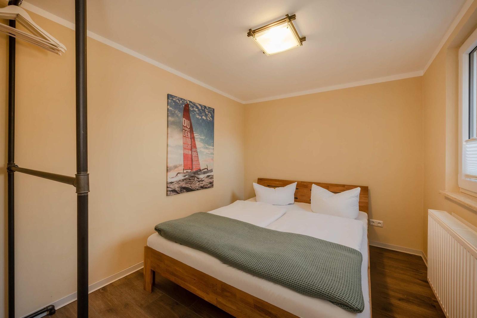 Schlafzimmer mit Bett, Wandbild und Kleiderständer.