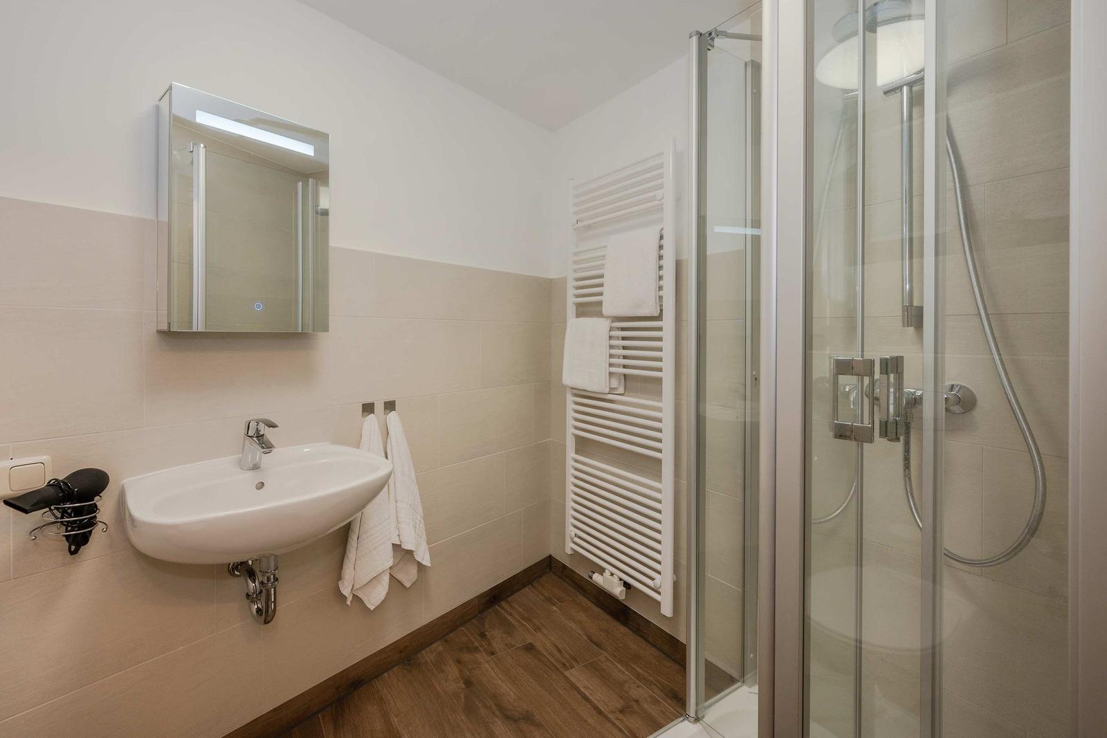 Badezimmer mit Dusche, Waschbecken und Heizkörper.