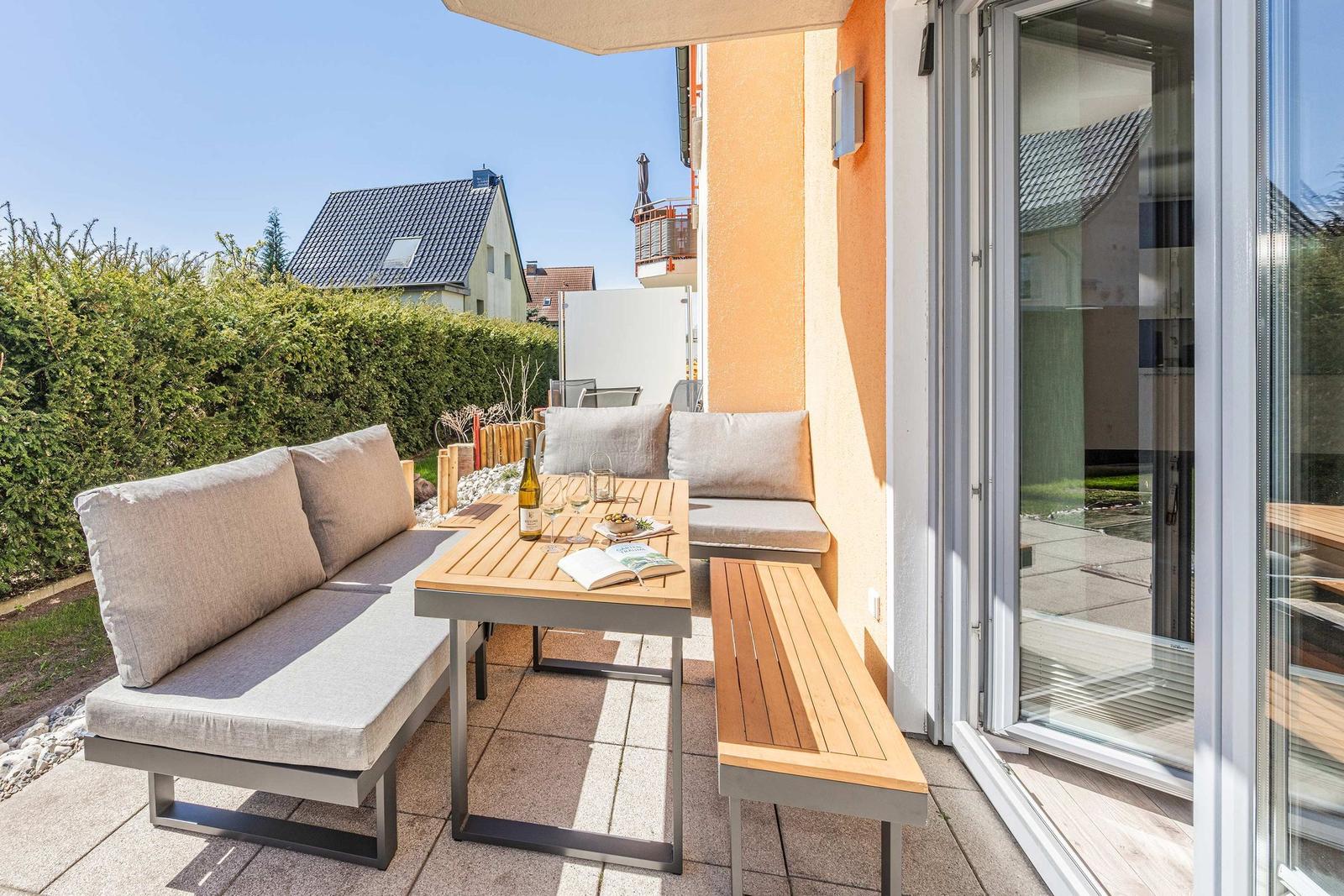 Terrasse mit Sitzgruppe, Tisch und Weinflasche. Blick auf grüne Hecke und Nachbarhäuser.