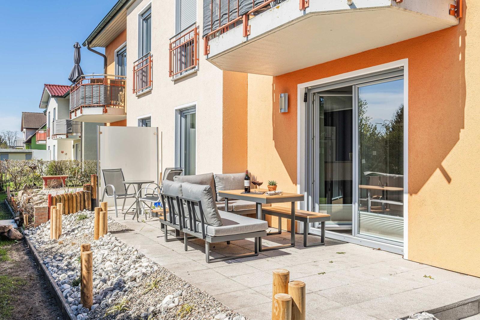 Terrasse mit Sitzgruppe, Tisch und Weinflasche vor orangefarbenem Haus.