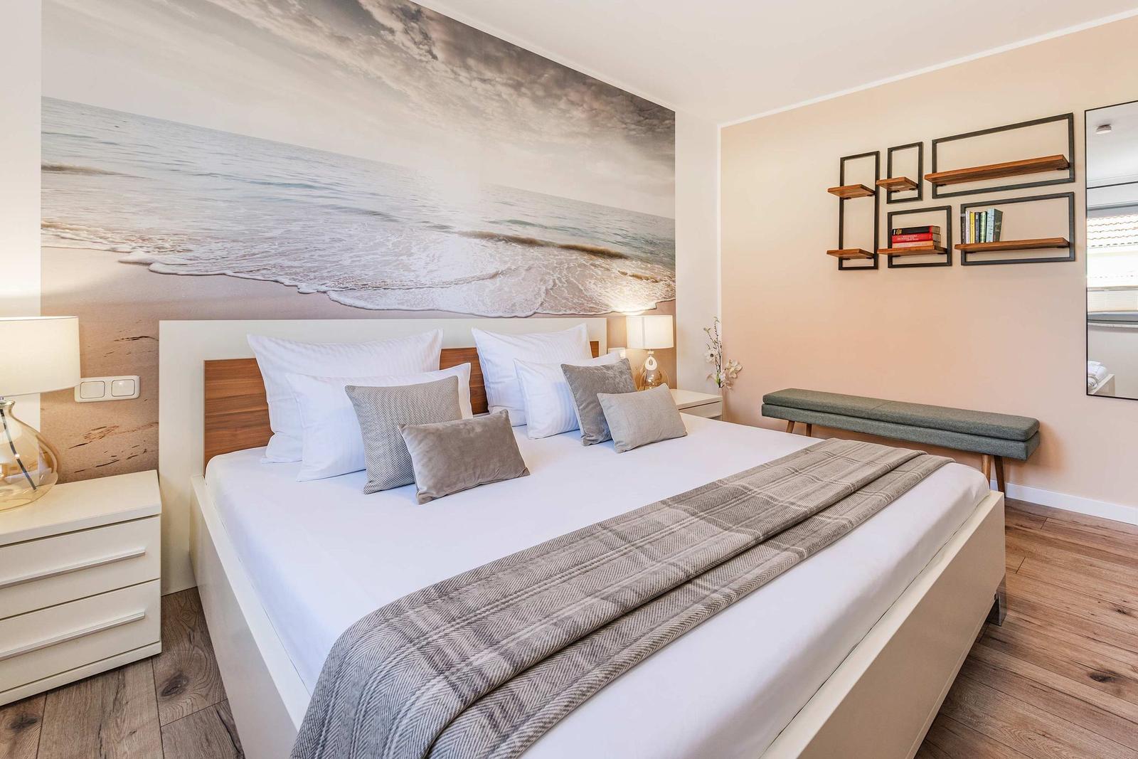 Schlafzimmer mit großem Bett, Strandbild an der Wand und Holzboden.