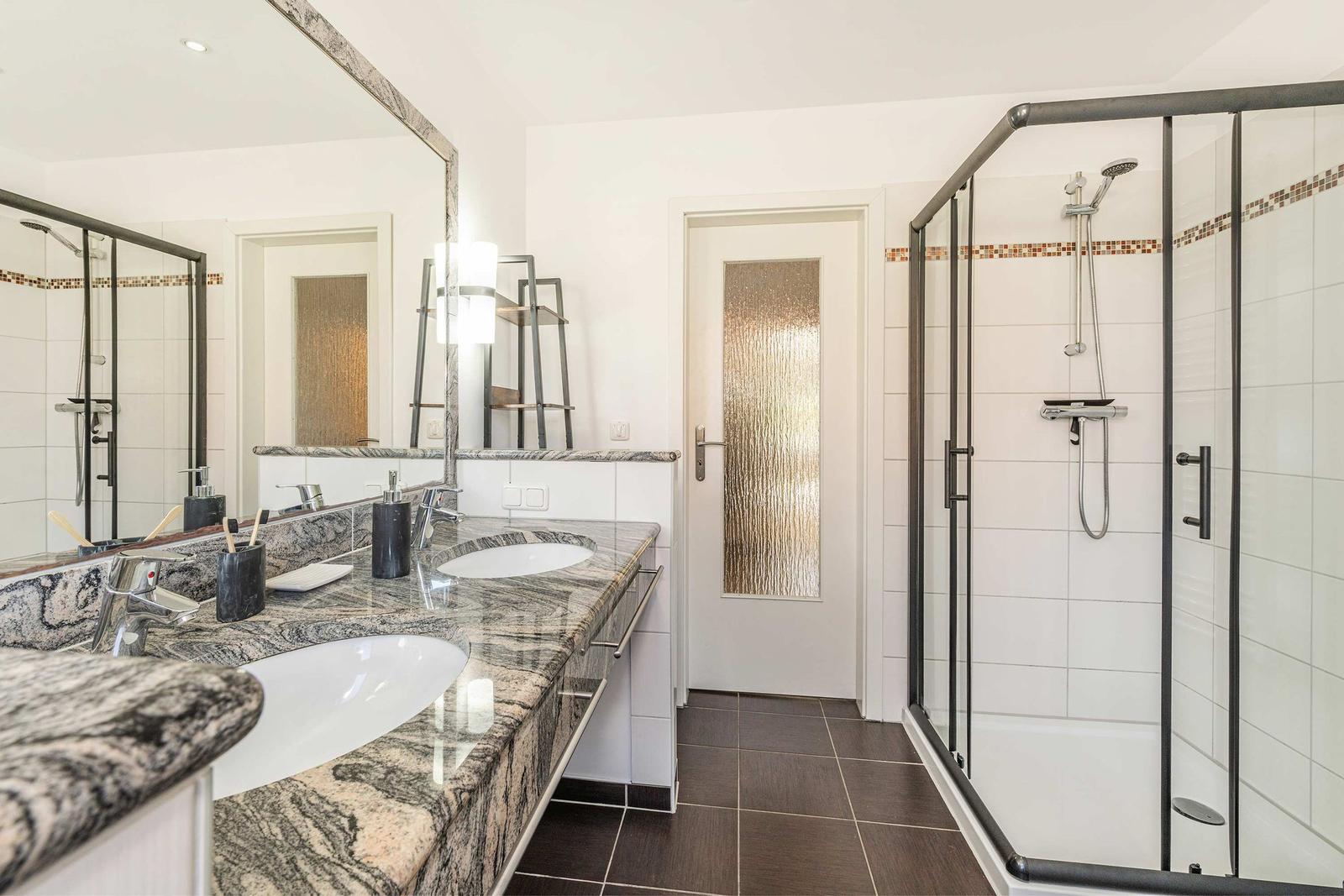 Badezimmer mit Dusche, Doppelwaschbecken und Marmorarbeitsplatte.