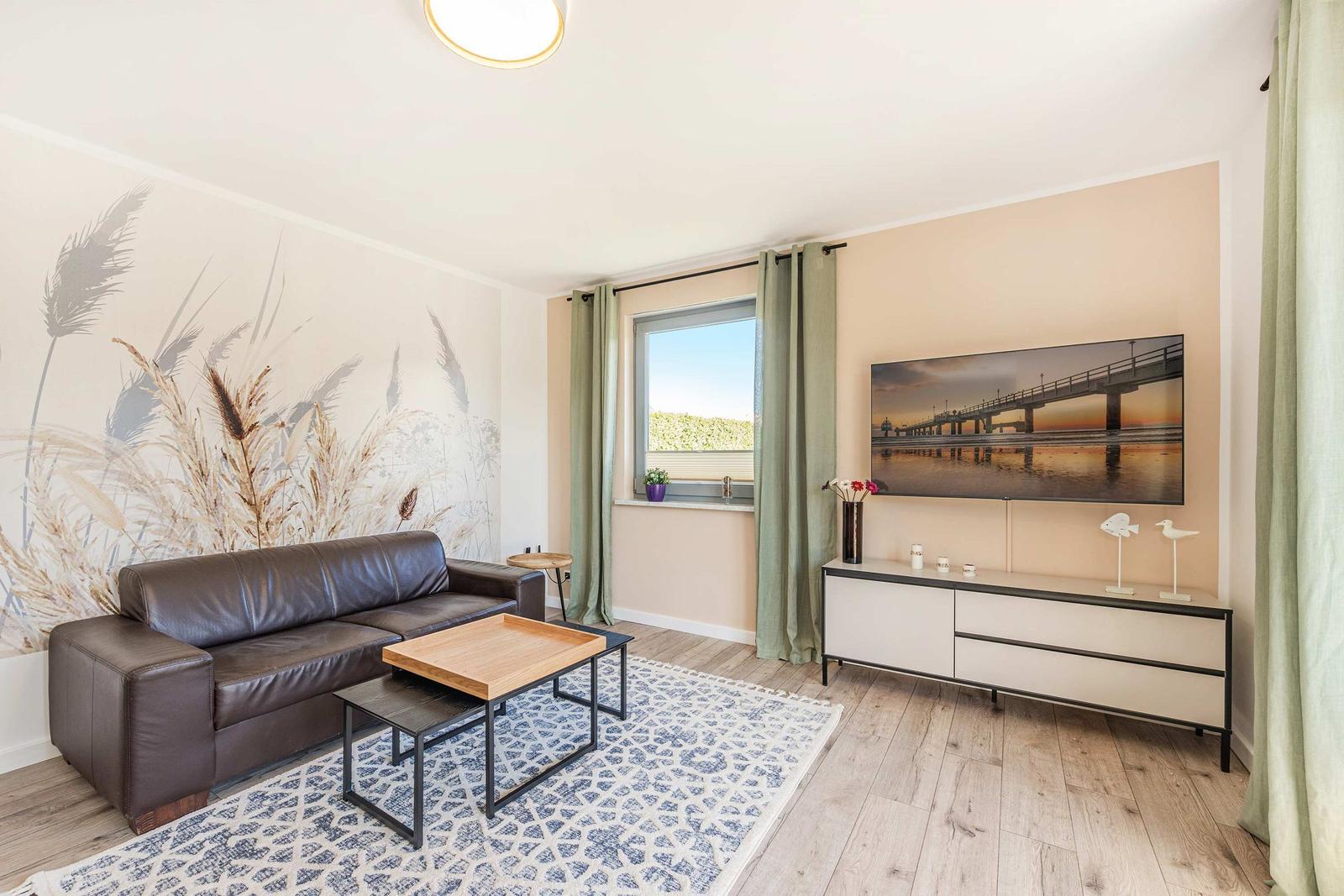 Wohnzimmer mit Ledersofa, Holztisch und Wandbild. Holzfußboden und Fenster mit Vorhängen.