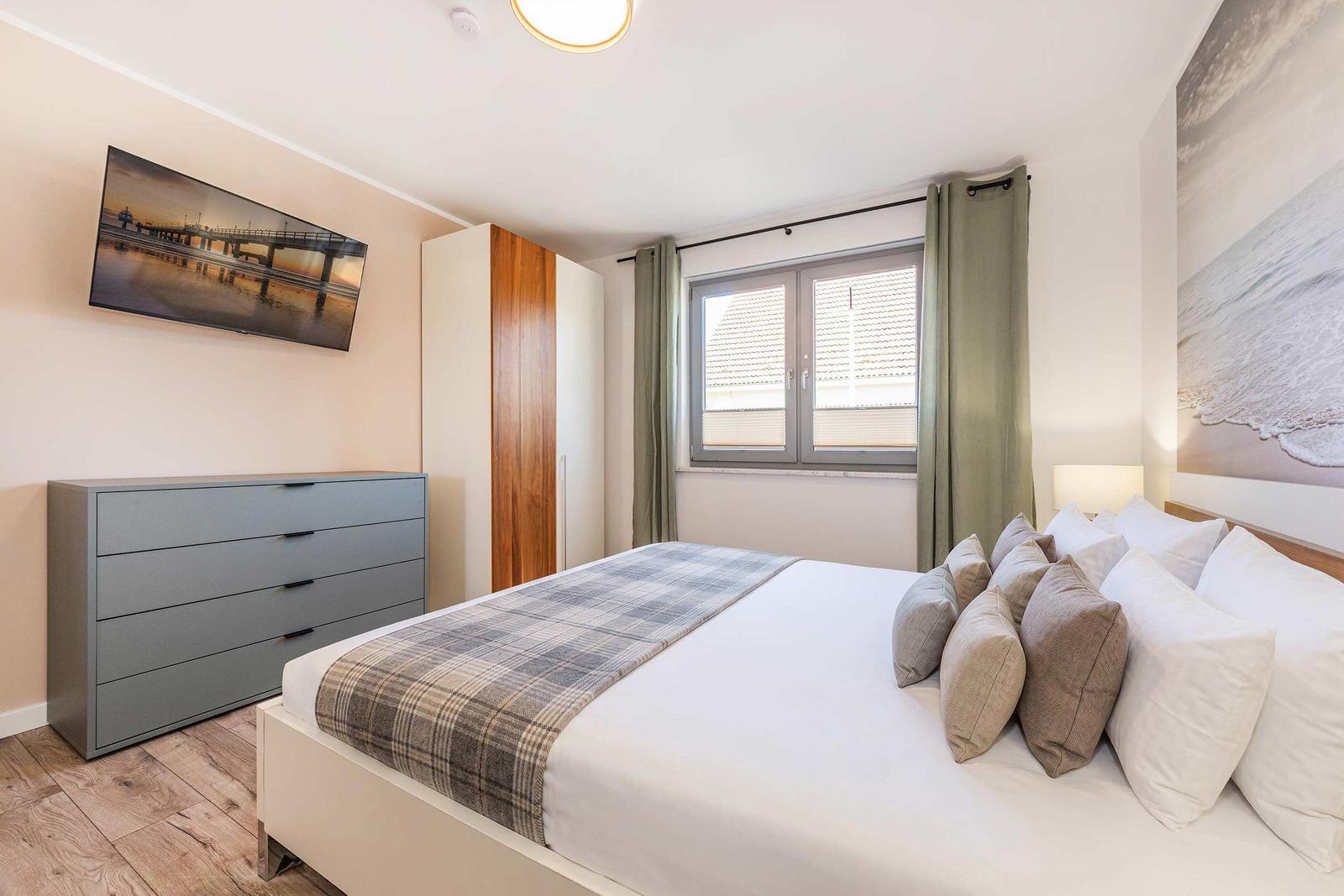 Schlafzimmer mit Bett, Schrank und Fenster. Wandbilder und Holzboden.