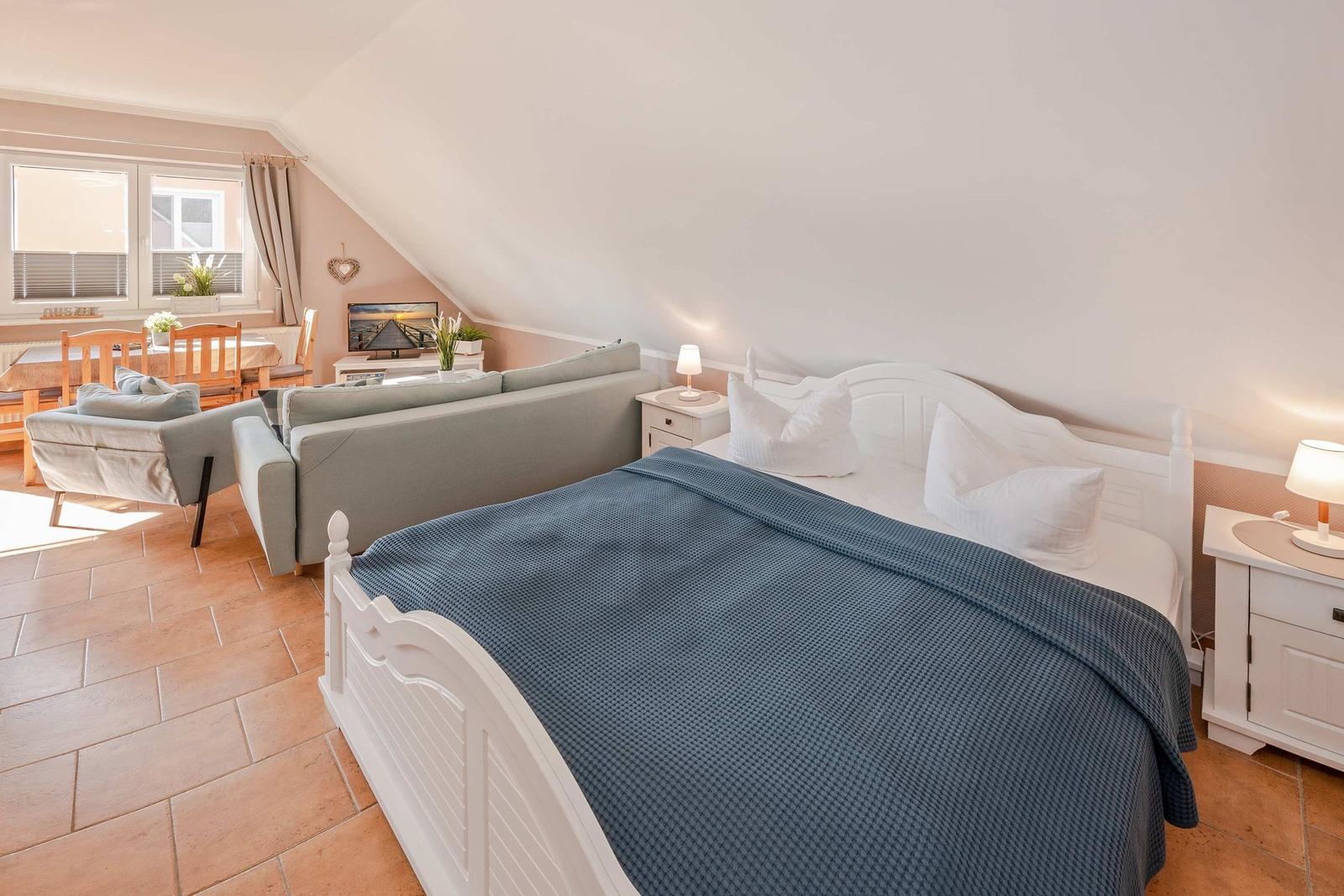 Schlafzimmer mit Doppelbett, Sofa und Essbereich unter Dachschräge.