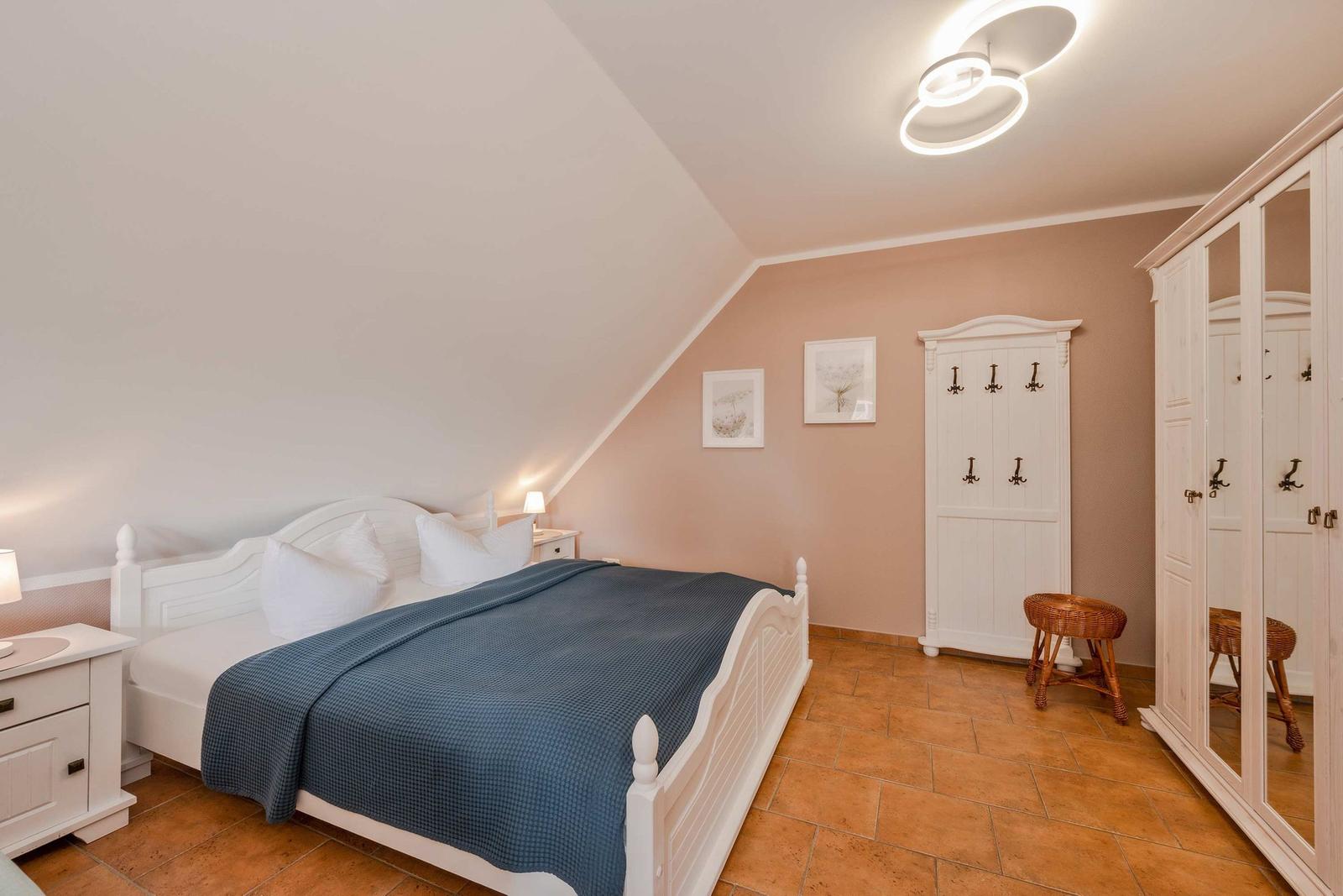 Schlafzimmer mit weißem Bett, blauer Decke, Schrank und Kleiderständer.