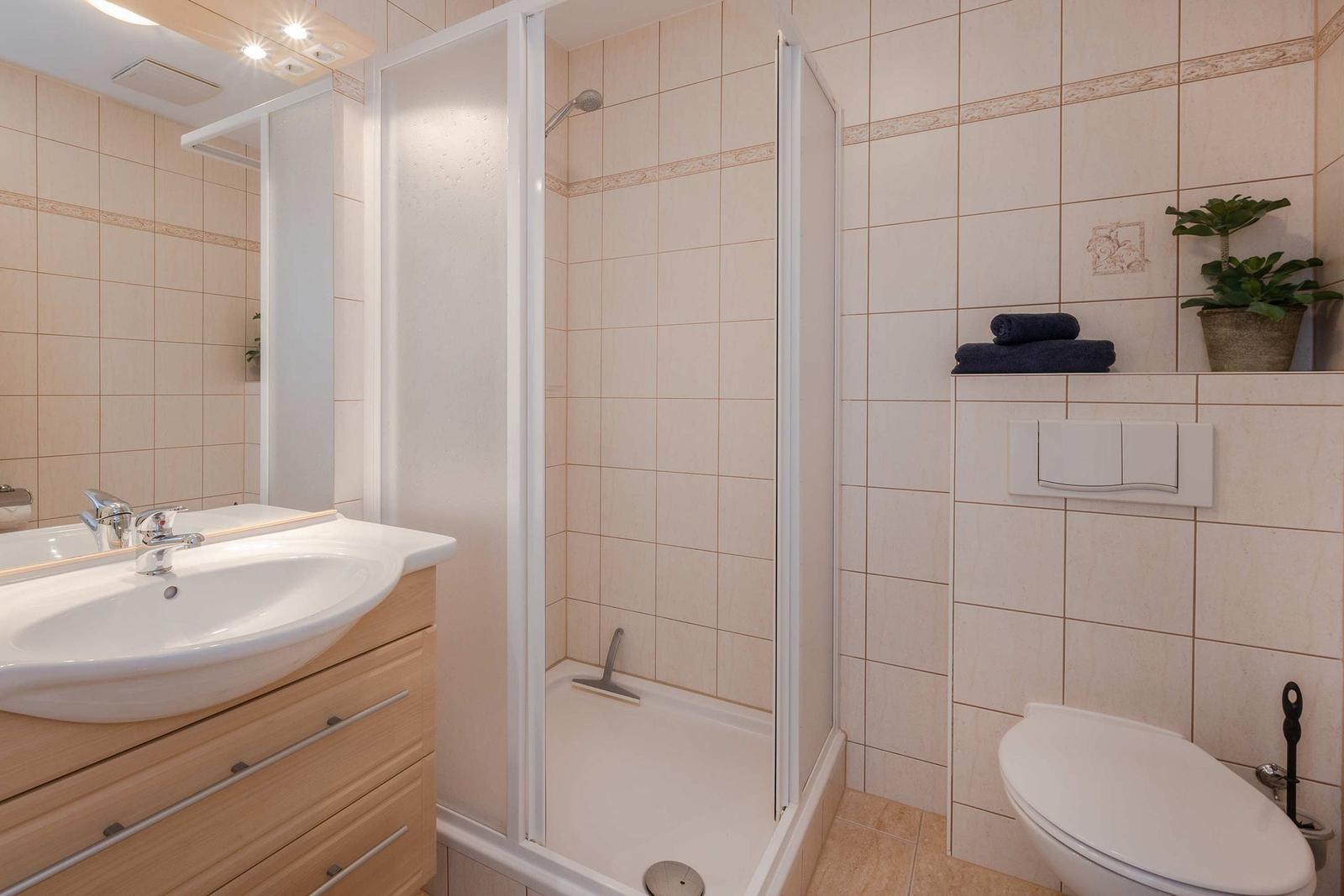 Bad mit Dusche, Waschbecken und Toilette. Fliesenwand und Holzschrank.
