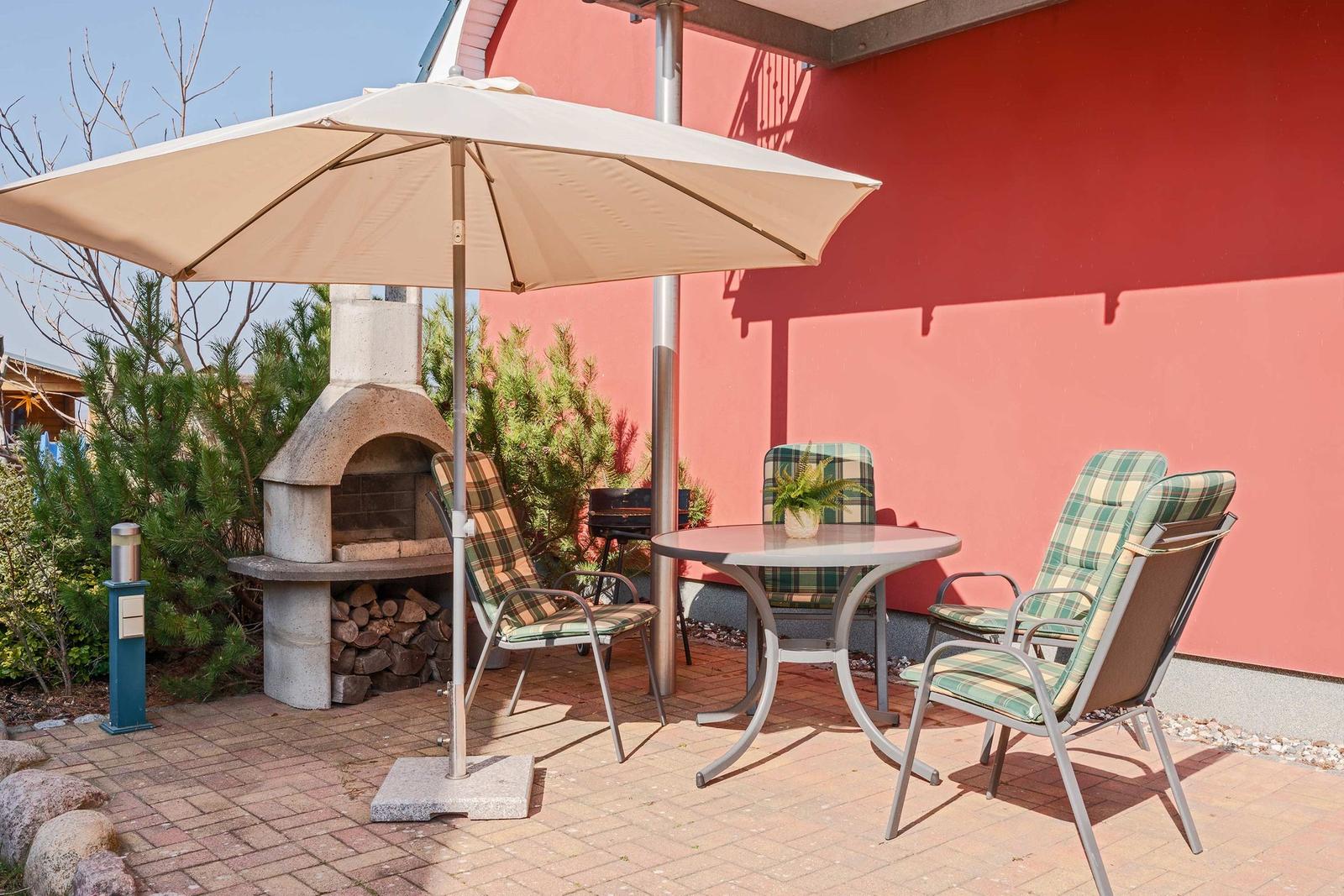 Terrasse mit Tisch, Stühlen, Sonnenschirm und Grillofen an roter Wand.