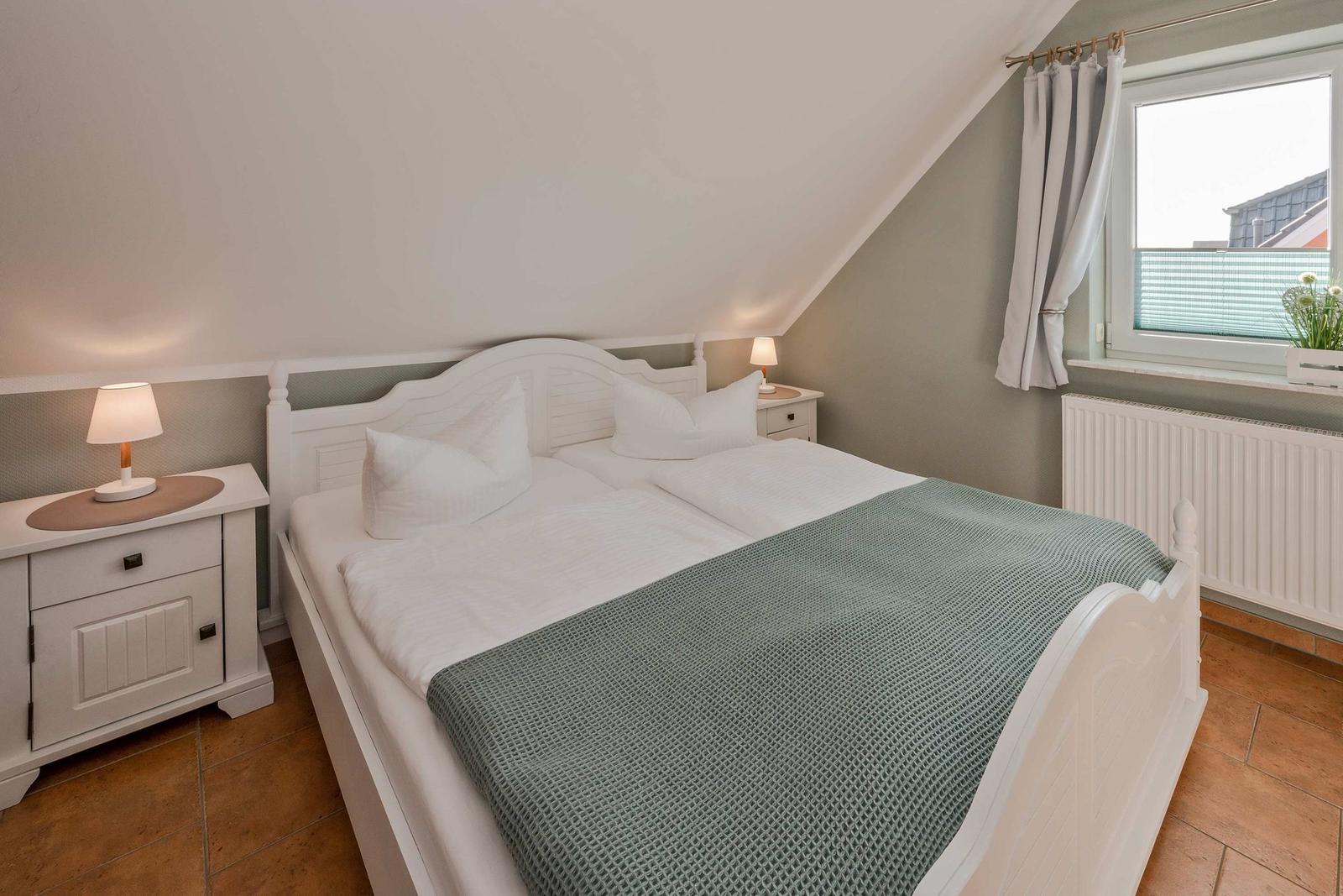 Schlafzimmer mit Doppelbett, zwei Nachttischen und Fenster mit Vorhang.
