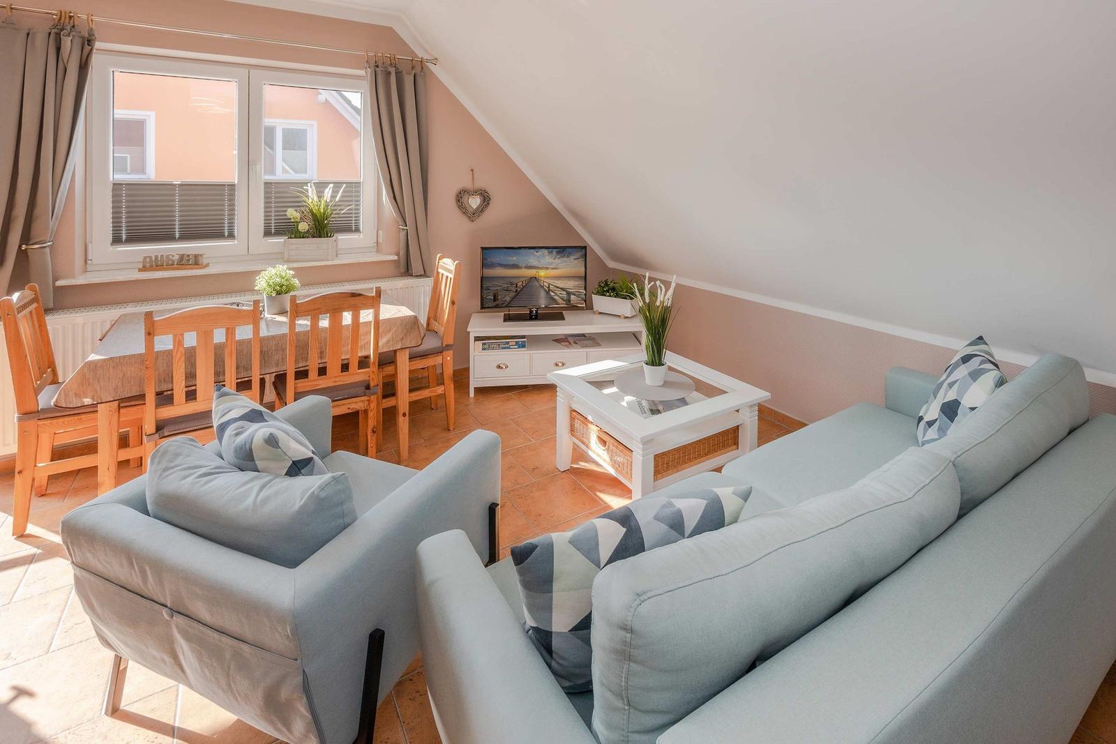 Wohn- und Essbereich mit Sofa, Sessel, Tisch und Fernseher unter Dachschräge.