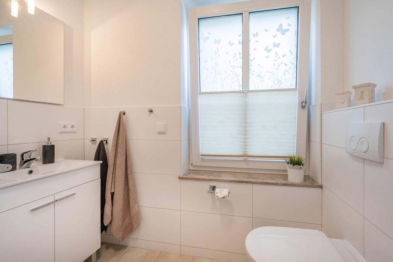 Badezimmer mit Waschbecken, Toilette und Fenster mit Schutzfolie.
