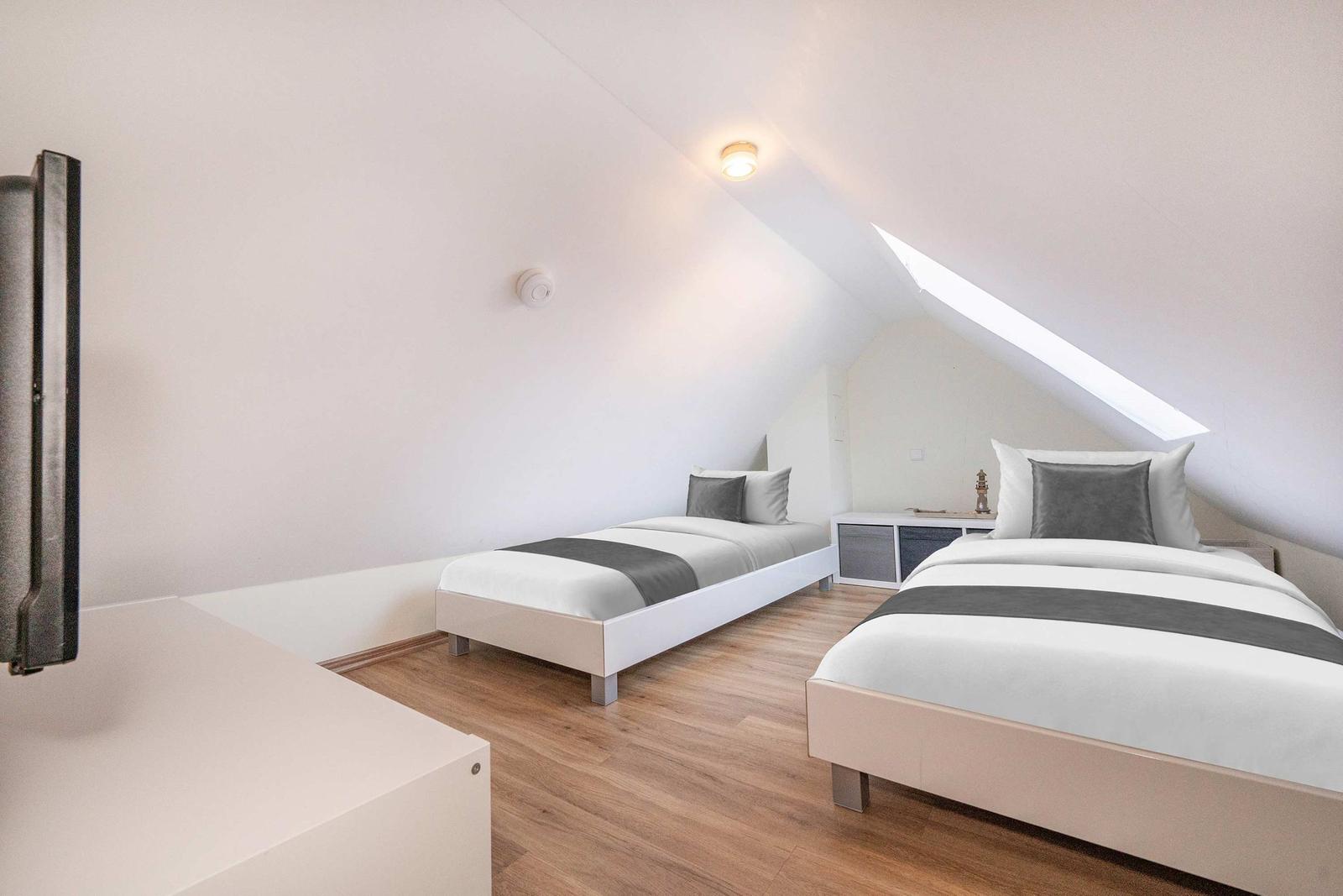 Zwei Betten in einem Dachzimmer mit Holzboden und Dachfenster.