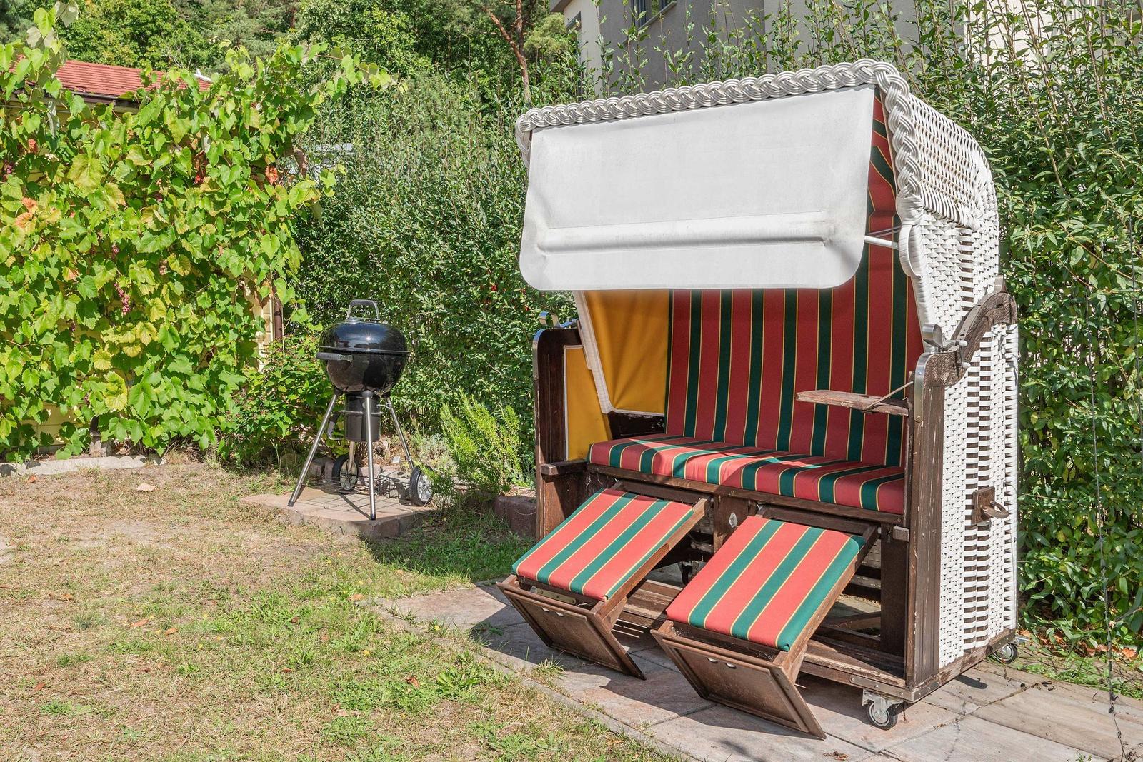 Hochwertiger Strandkorb mit Streifenbezug und Grill im Garten.