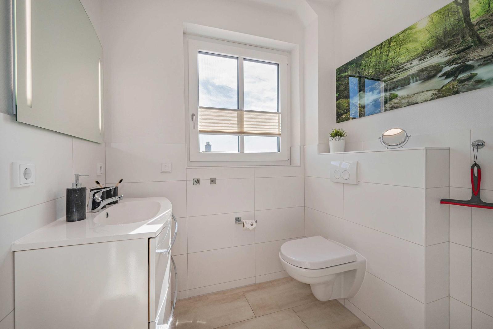 Badezimmer mit Waschbecken, Toilette und Fenster mit Jalousie.