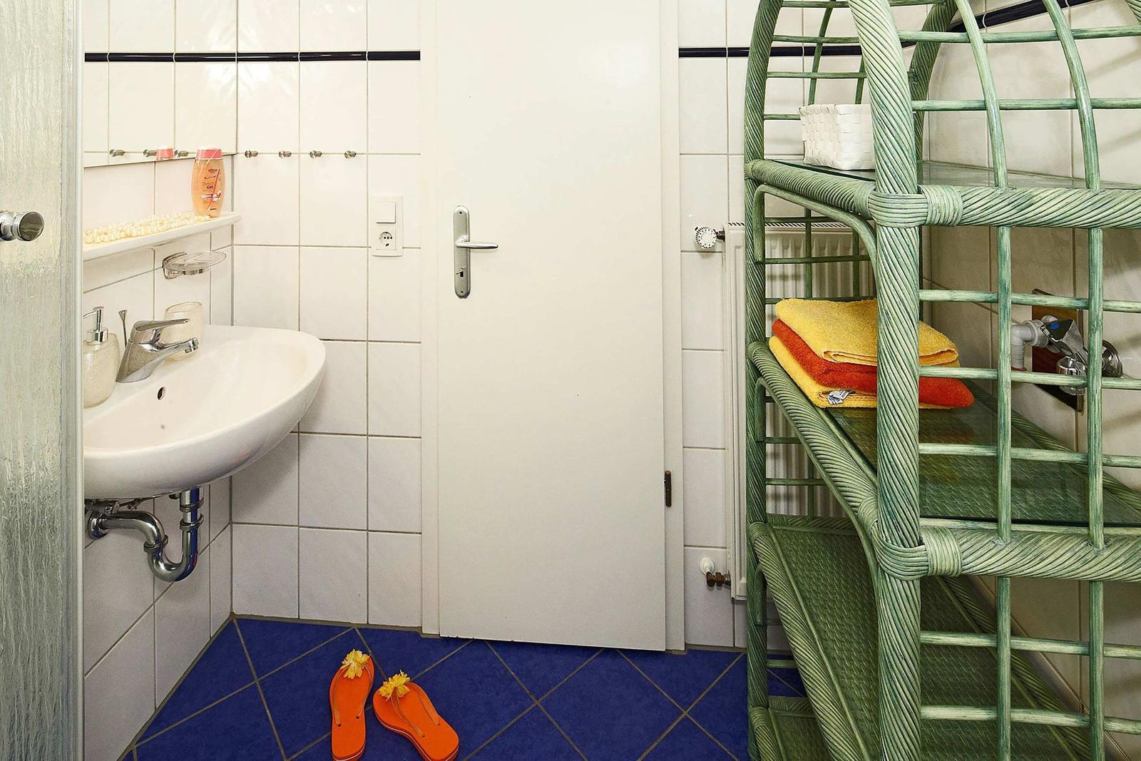 Badezimmer mit Waschbecken, Spiegel und grünem Regal mit Handtüchern.