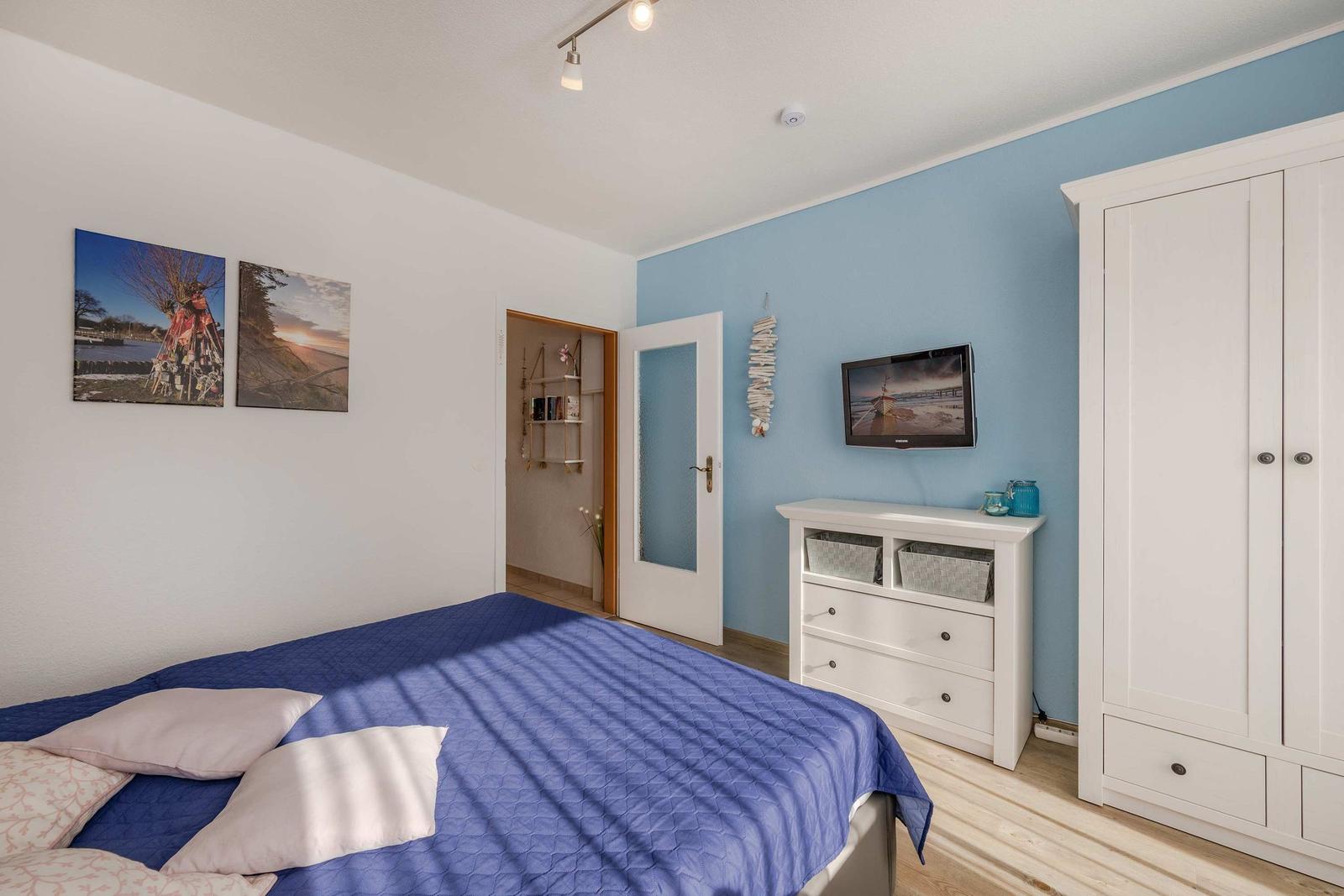 Schlafzimmer mit Bett, Kleiderschrank und Fernseher an blauer Wand.