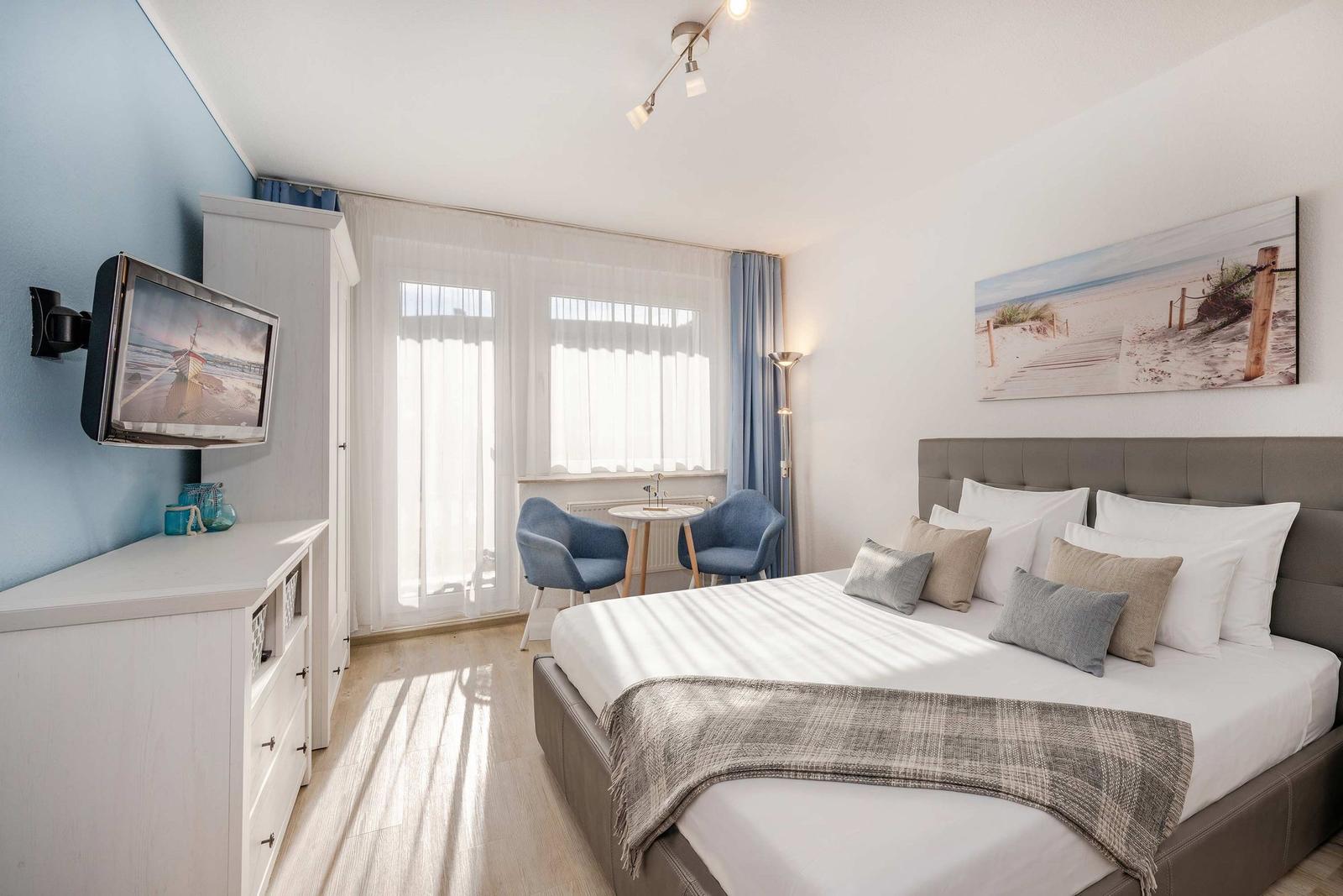 Schlafzimmer mit Bett, TV und Fenster. Wandbild und Möbel sind sichtbar.