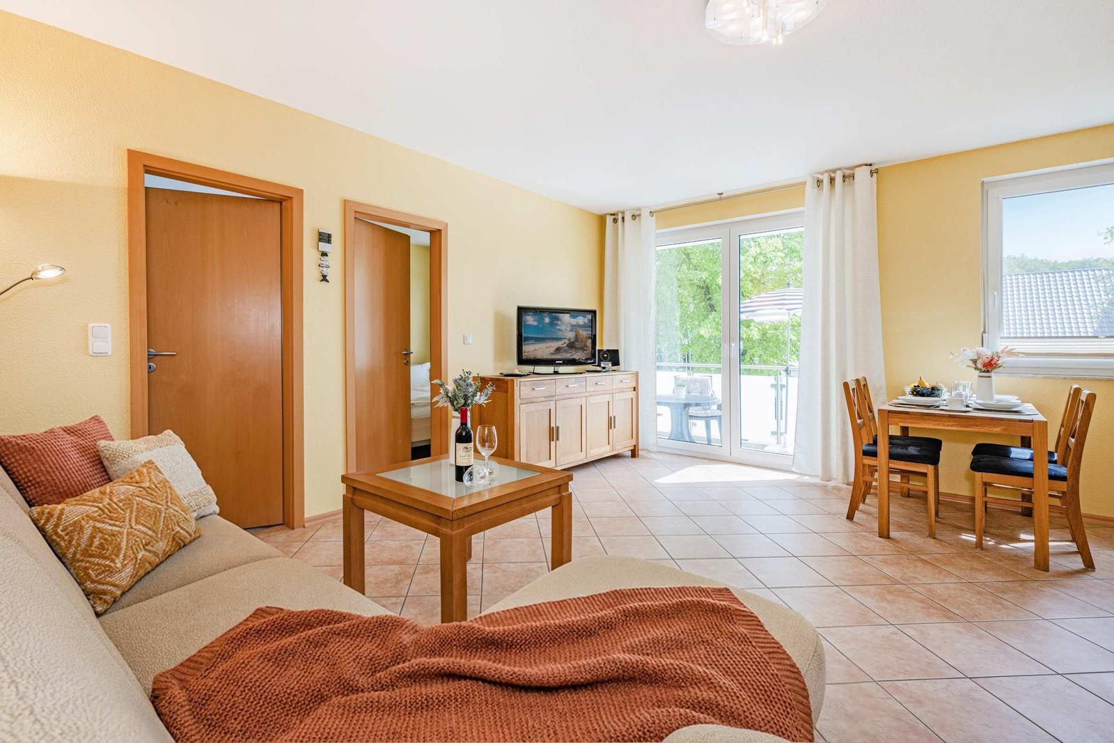 Wohn- und Essbereich mit TV, Terrasse und Essgruppe. Holzmöbel und warme Wandfarbe.