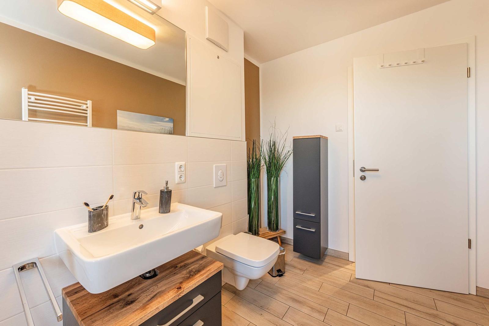 Badezimmer mit Waschbecken, Toilette und Spiegelschrank. Holzoptik und moderne Einrichtung.