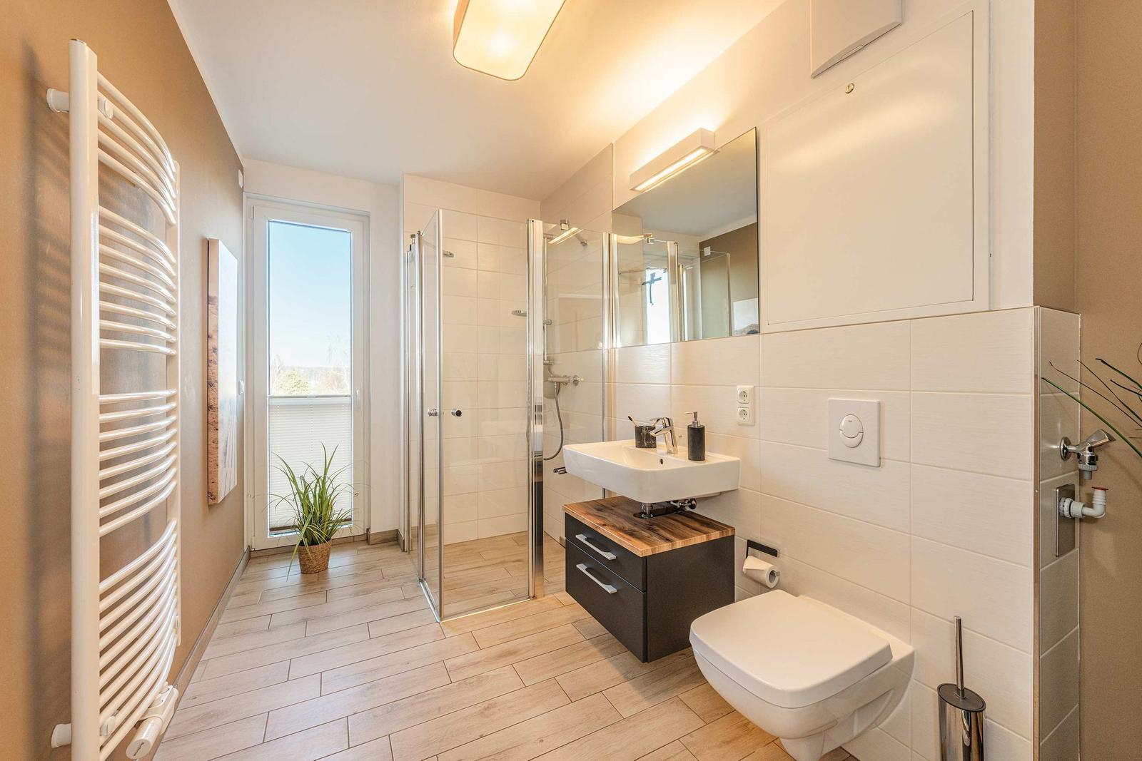 Badezimmer mit Dusche, Waschbecken und Toilette. Fenster mit Blick nach draußen.