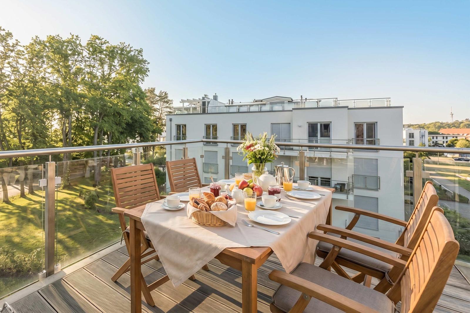 Terrasse mit Tisch, Stühlen und Frühstück. Blick auf Gebäude und Bäume.