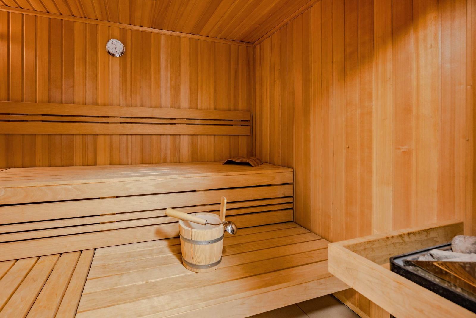 Sauna mit Holzbank, Thermometer und Eimer mit Löffel.