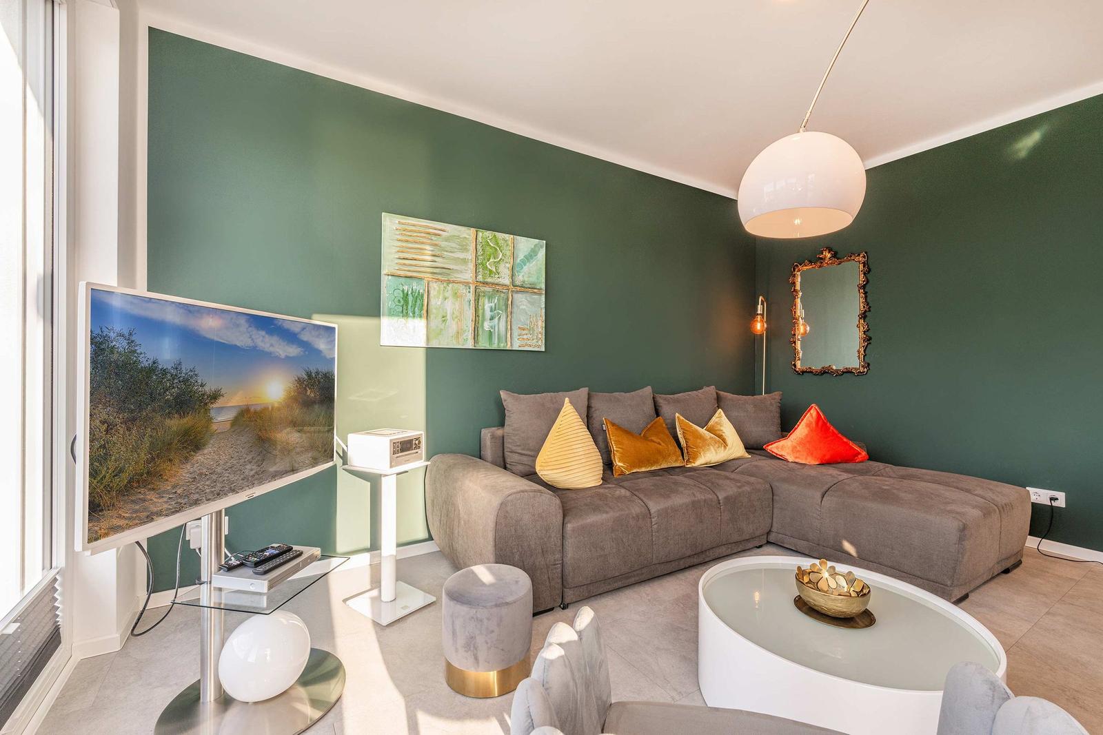 Ein Wohnzimmer mit grüner Wand, grauem Sofa und runden Möbeln.