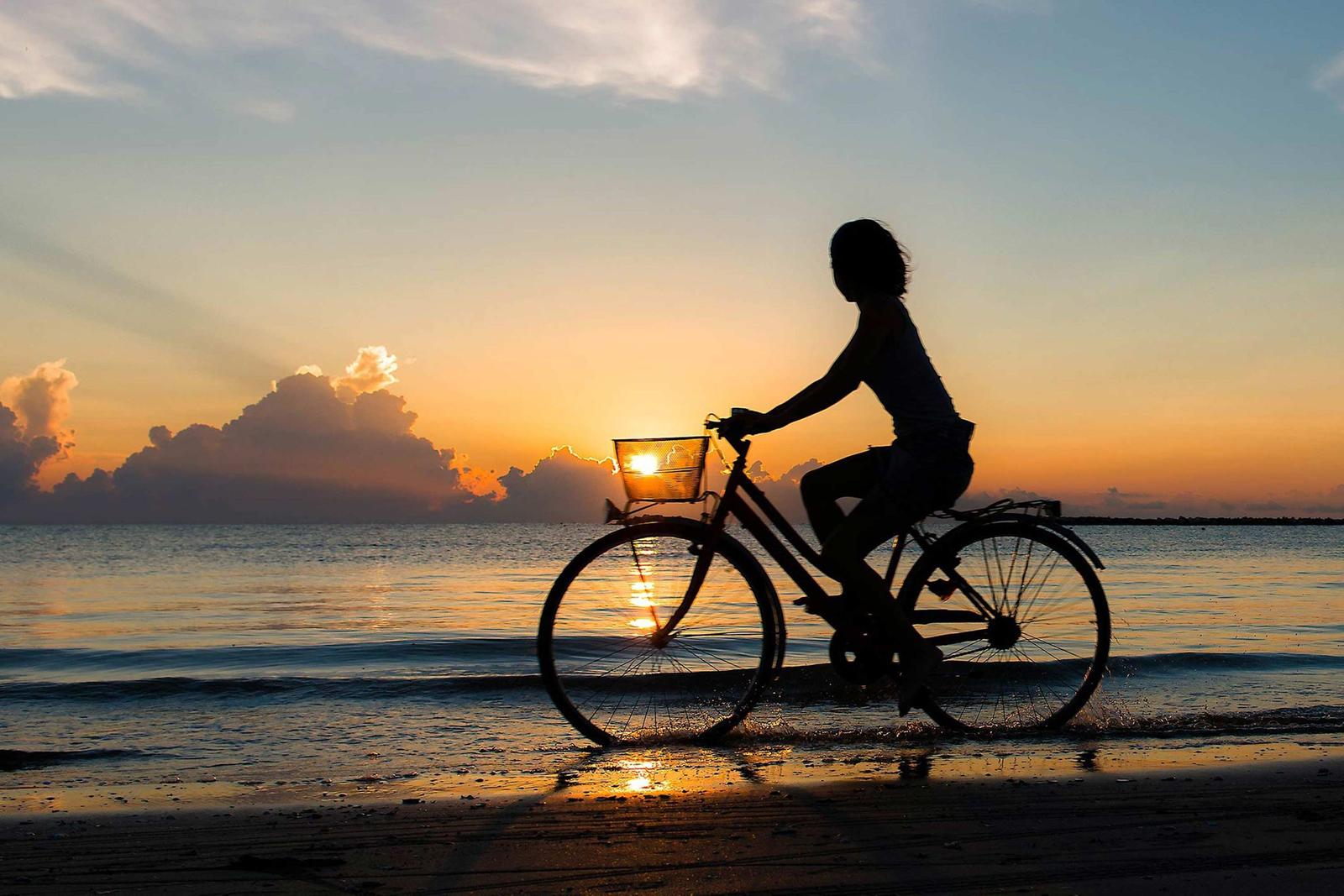 Silhouette einer Person auf einem Fahrrad am Strand bei Sonnenuntergang.