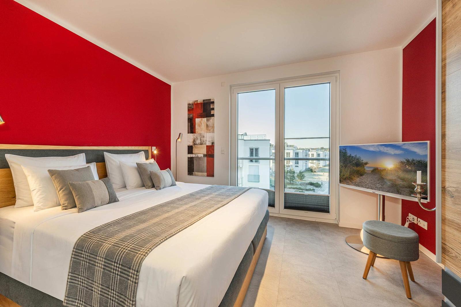 Schlafzimmer mit großem Bett, roten Wänden und Blick auf Außenbereich.