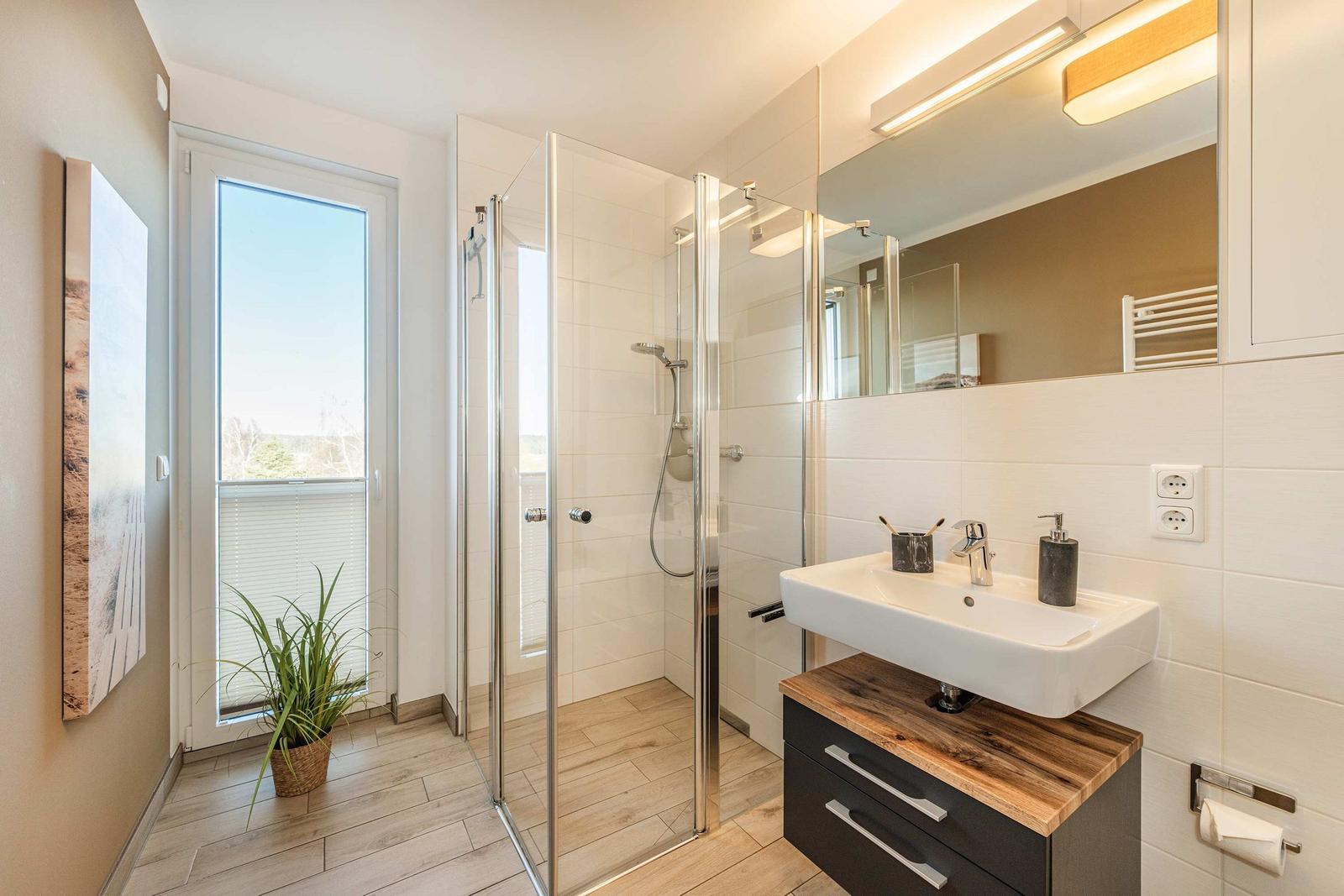 Badezimmer mit Dusche, Waschbecken und Fenster. Holzboden und Wandfliesen.
