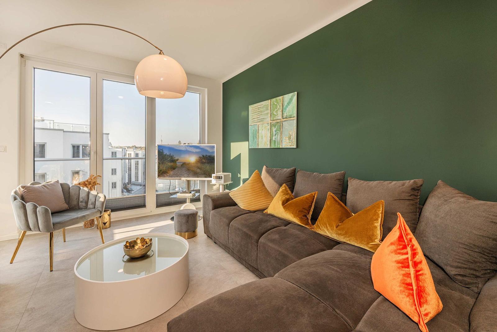 Wohnzimmer mit Sofa, Couchtisch und großem Fenster. Grüne Wand und dekorative Kissen.