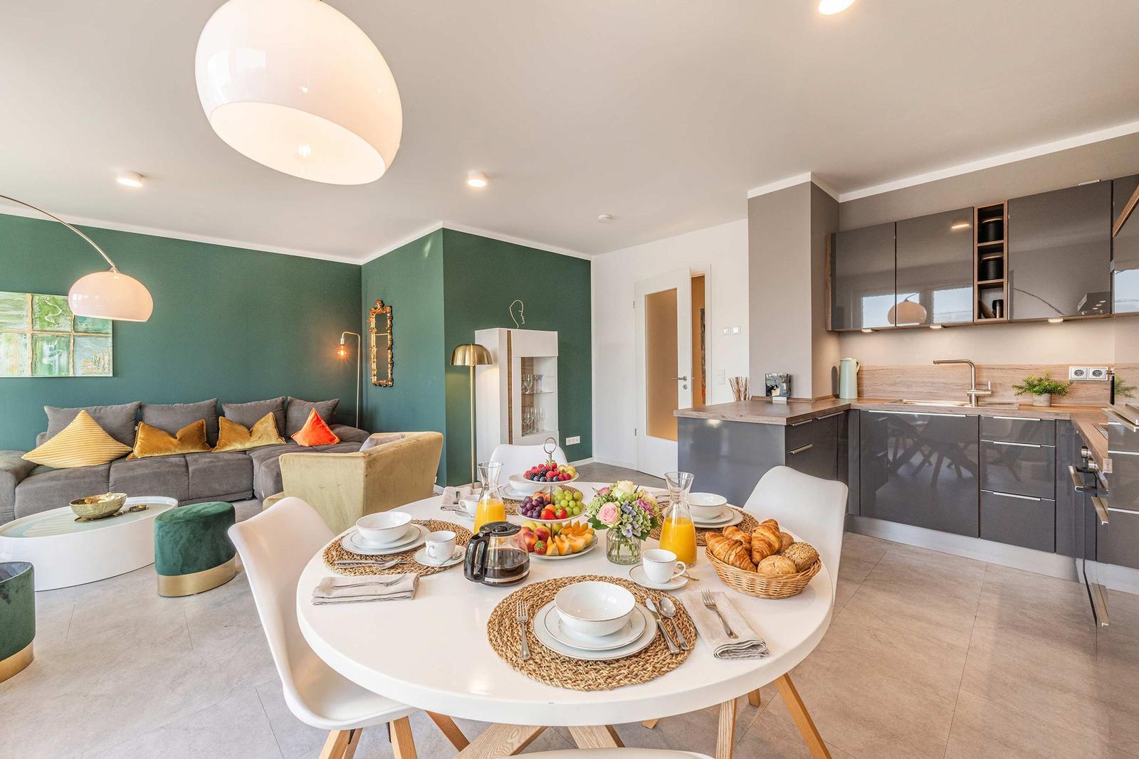 Esszimmer mit Frühstück, Küche und Wohnzimmer mit grüner Wand und Sofa.