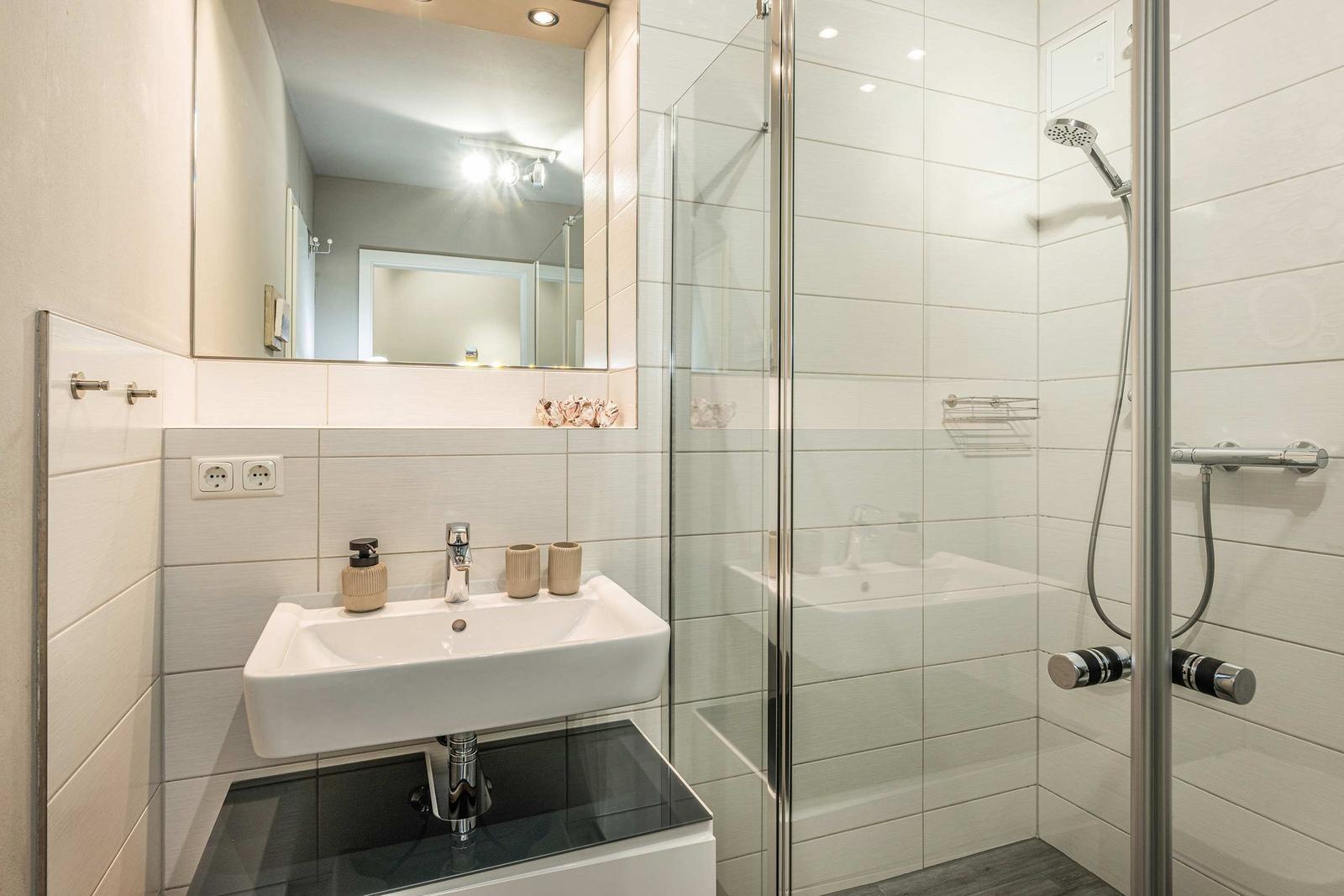 Badezimmer mit Dusche, Waschbecken und Spiegel.