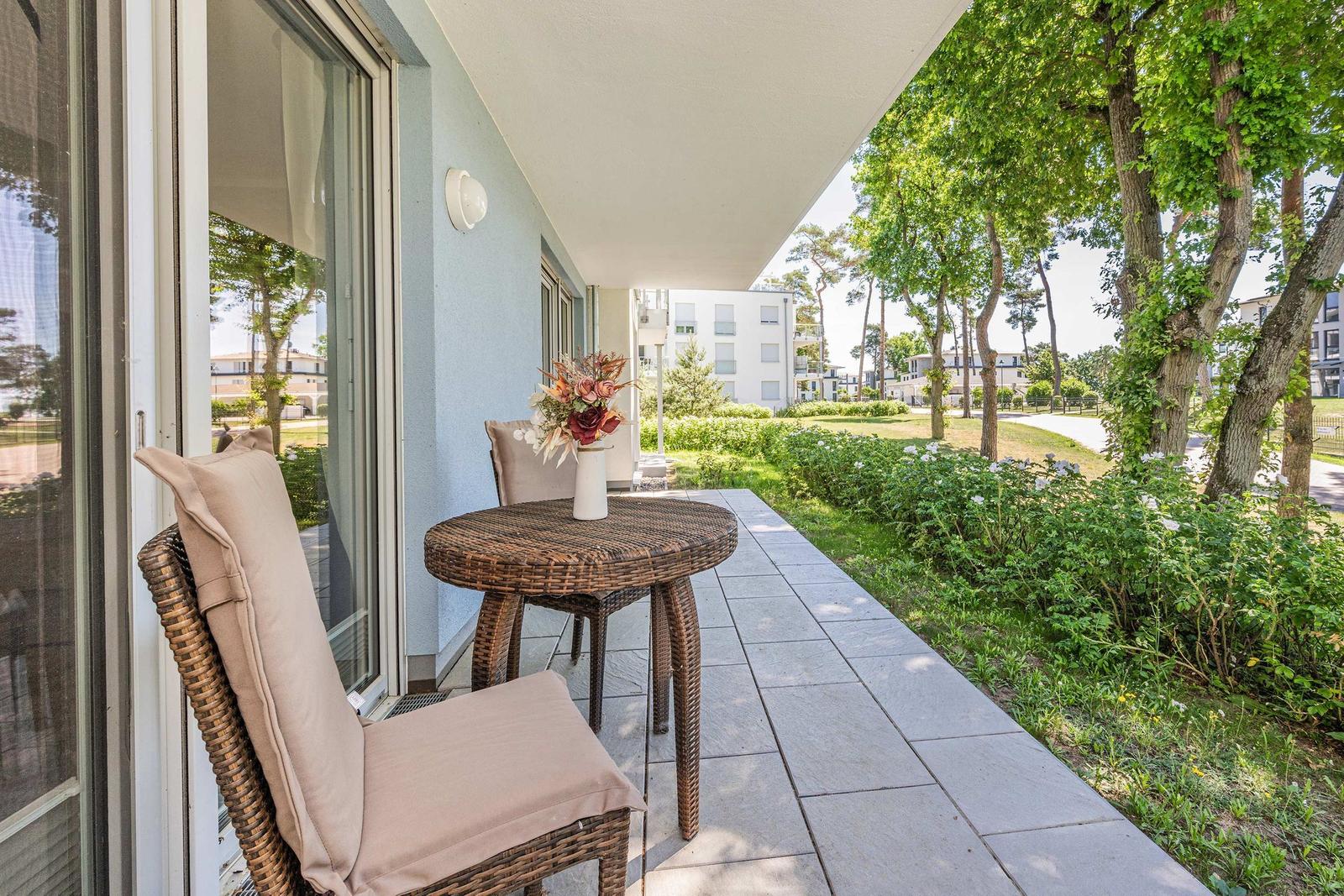 Terrasse mit Tisch und Stühlen, Blick auf grüne Bäume und Wohngebäude.